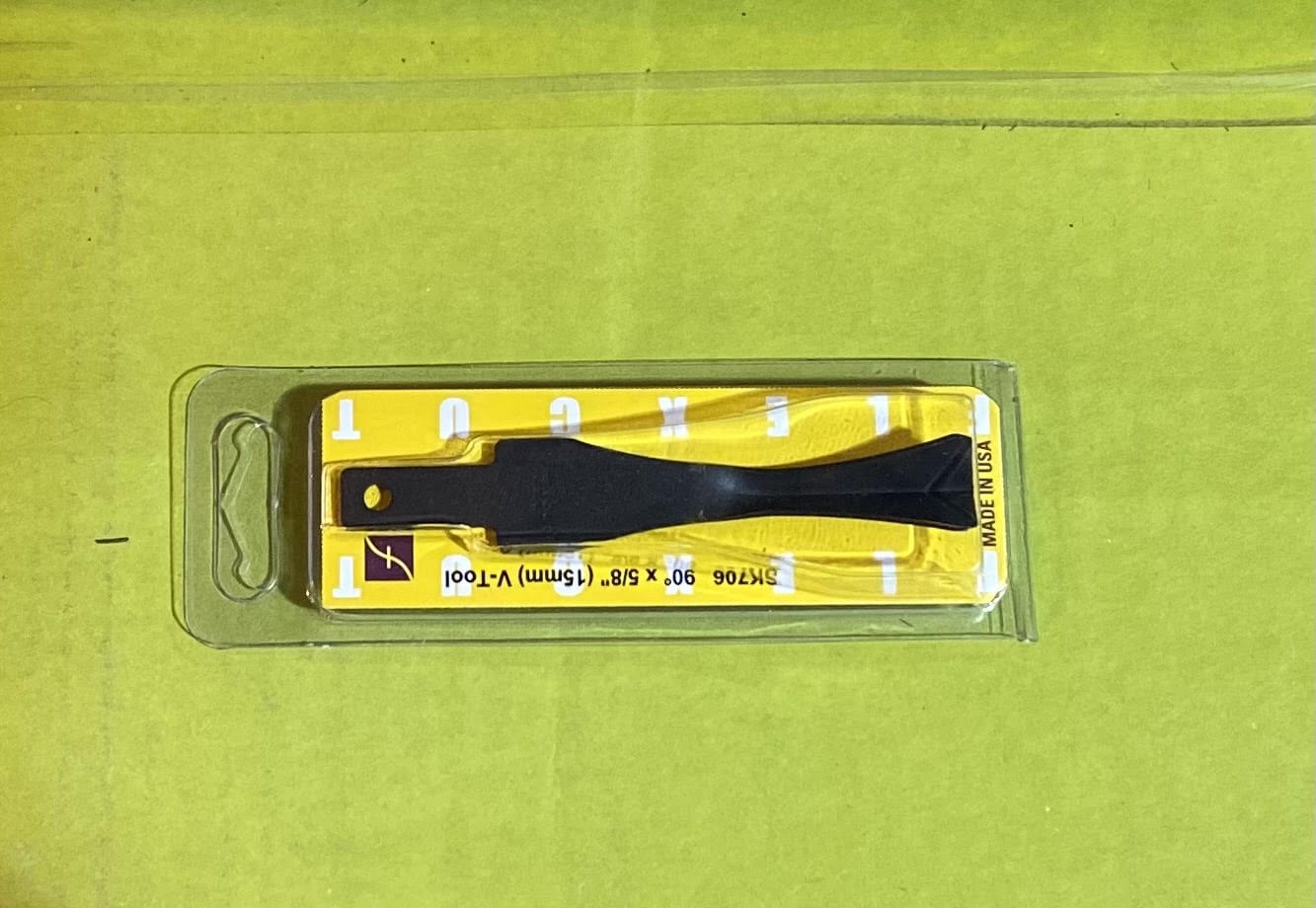 A small black FLE 5/32-IN x 45 DEGREES V-Tool Blade in clear packaging with a yellow and white MADE IN USA label, shown on a bright green background. Handle sold separately; product info on label.