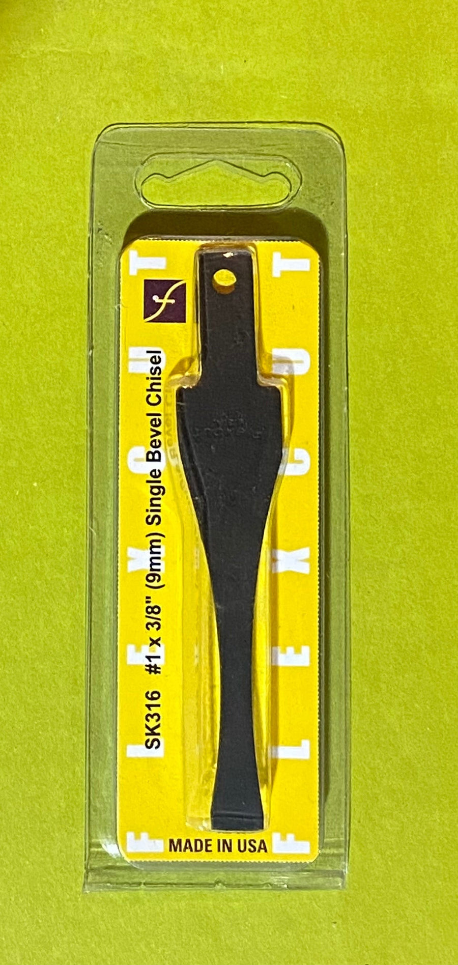 A Flexcut Blade 3/8-in. Chisel from FLE is shown in clear plastic packaging with a yellow FLEXCUT and MADE IN USA label, set against a green background.