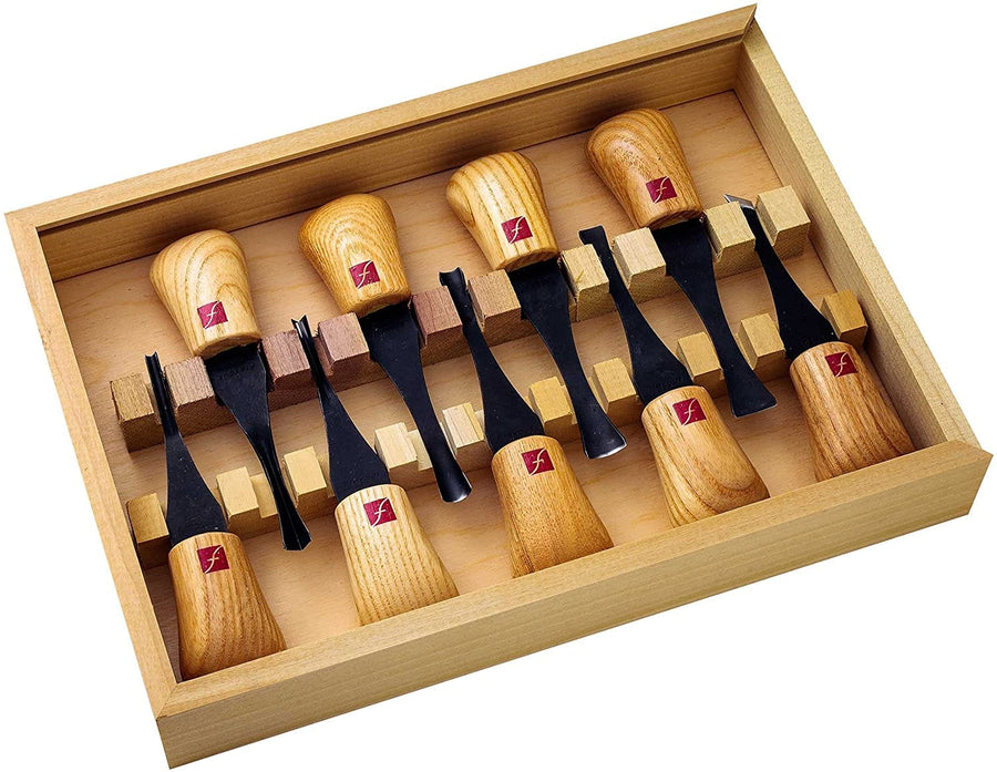 The Flexcut Deluxe Palm Set 9pc by FLE features nine palm carving tools with ergonomic light brown handles and durable carbon steel blades, each chisel held securely by a wooden divider in a wooden box.