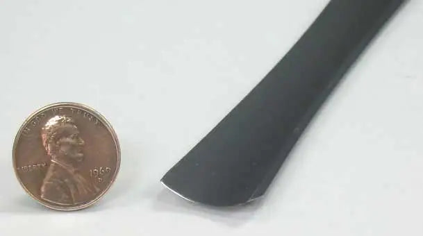 A 1969 U.S. penny is placed beside the FLE Mallet Gouge, a black, flat, slightly curved handcrafted tool, on a white surface for size comparison.