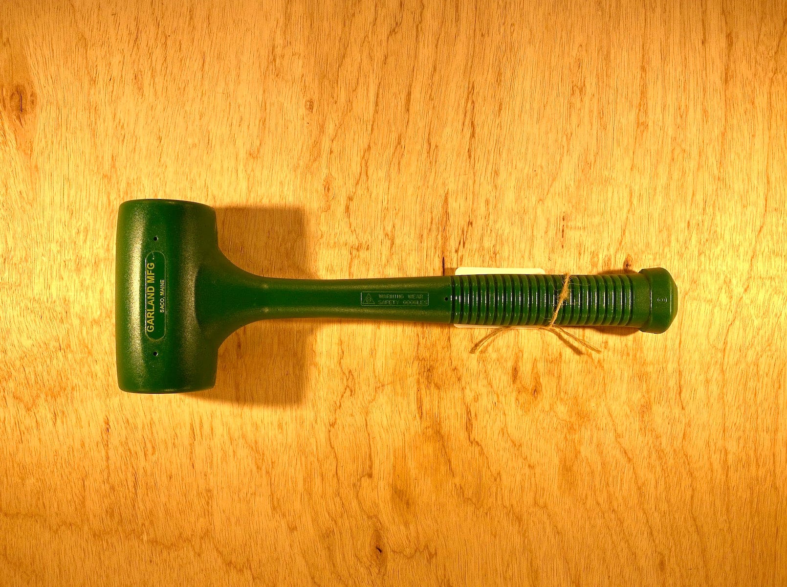 The Garland Dead Blow Mallet by GAM, featuring a textured handle and made from cast polyurethane, sits on a wooden surface.