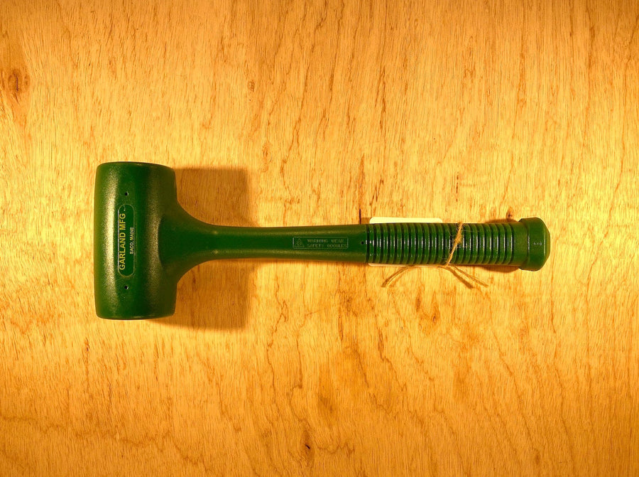 The Garland Dead Blow Mallet by GAM, featuring a textured handle and made from cast polyurethane, sits on a wooden surface.