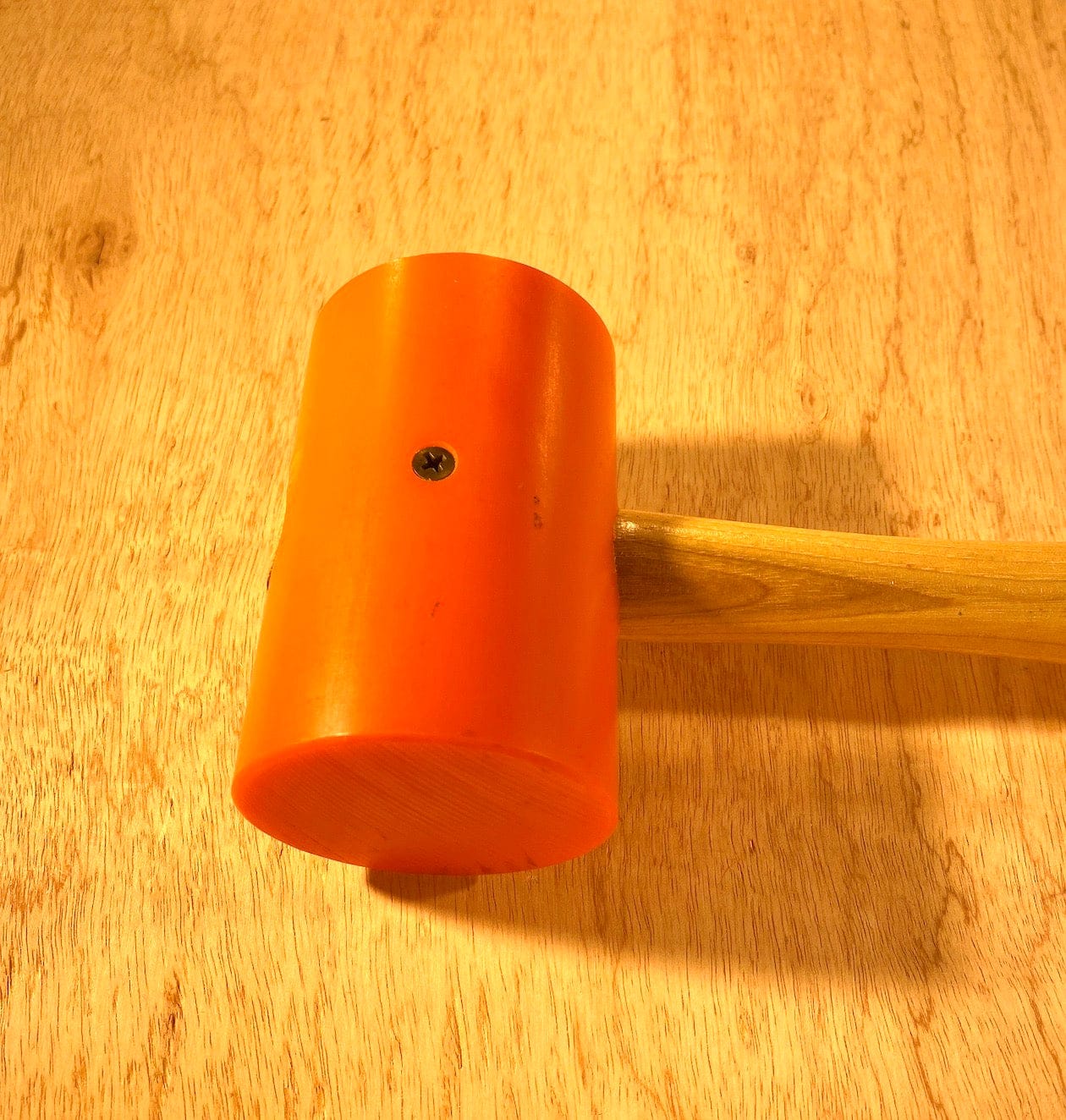 The GAM Garland Elastomer Mallet, featuring an orange head and a wooden handle, rests on a wooden surface, perfect for die-making applications.
