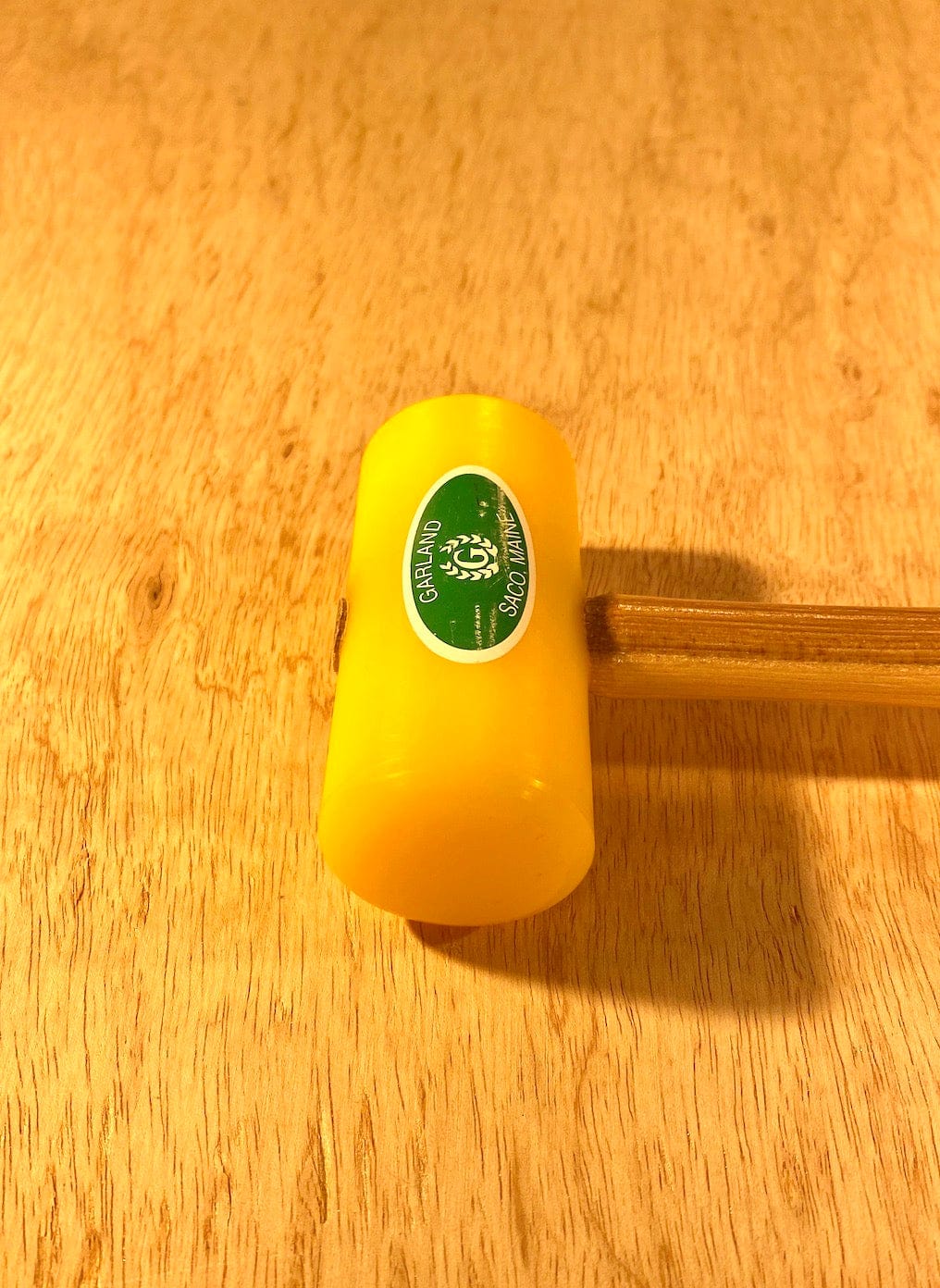 The Garland Plastic Mallet by GAM, featuring a yellow head made from ultra-high-molecular-weight plastic and a wooden handle, rests on a wooden surface. It has a green and white sticker labeled "3300" and is easy to clean, making it perfect for various tasks.