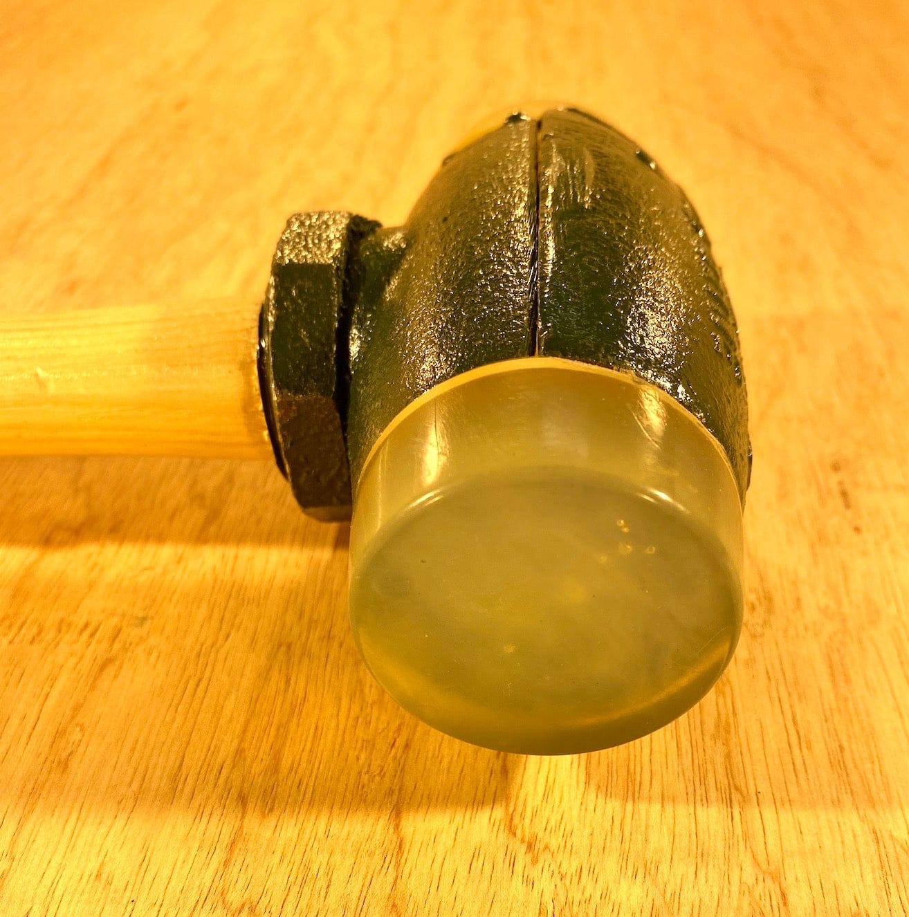 A Split Head Hammer Urethane Face by GAM, featuring a metal head with interchangeable faces, sits on a wooden surface.