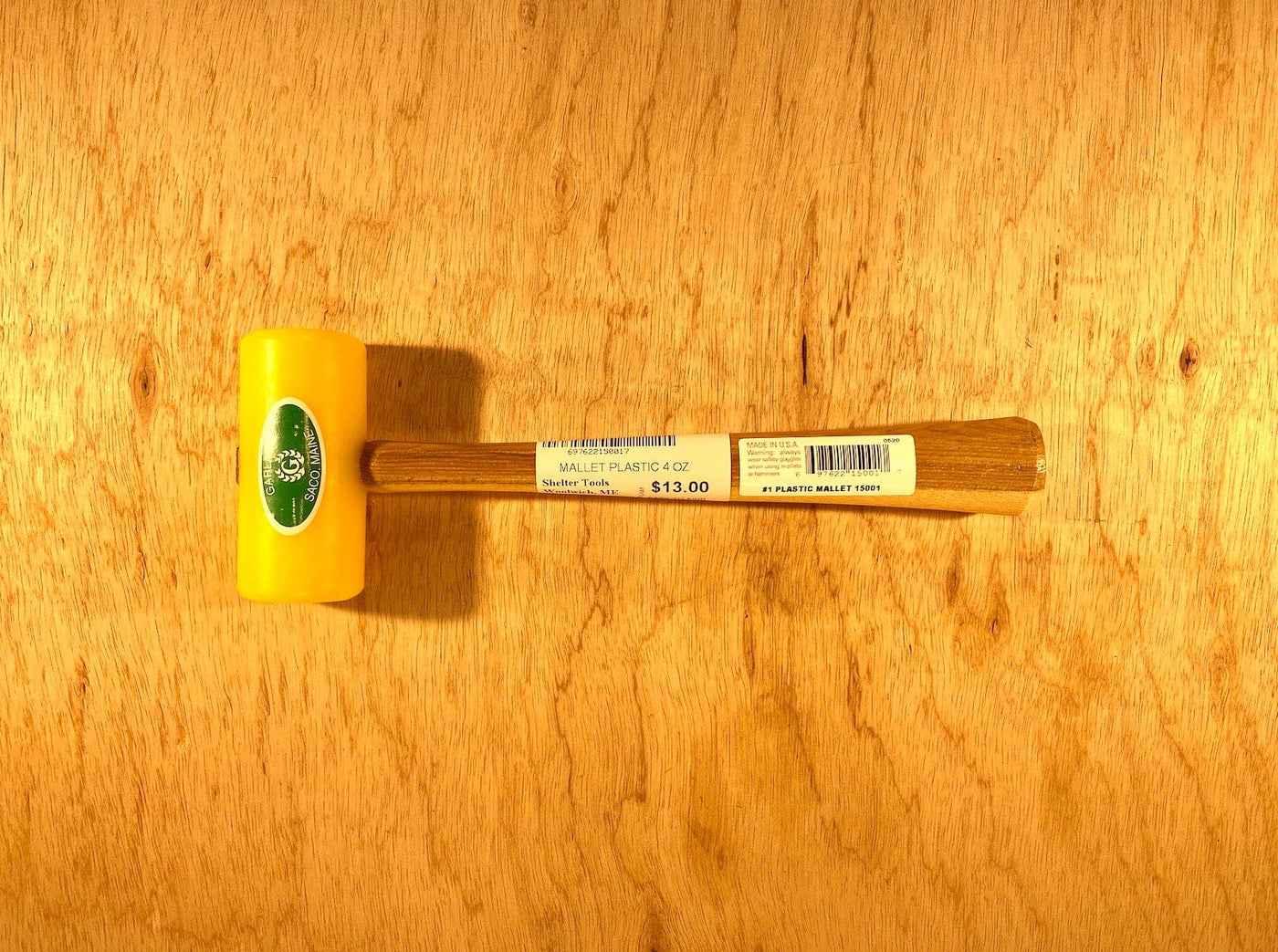 The Garland Plastic Mallet by GAM, featuring a yellow head made from ultra-high-molecular-weight plastic for durability and ease of cleaning, paired with a wooden handle, is priced at $13.00 and placed on a wooden surface.