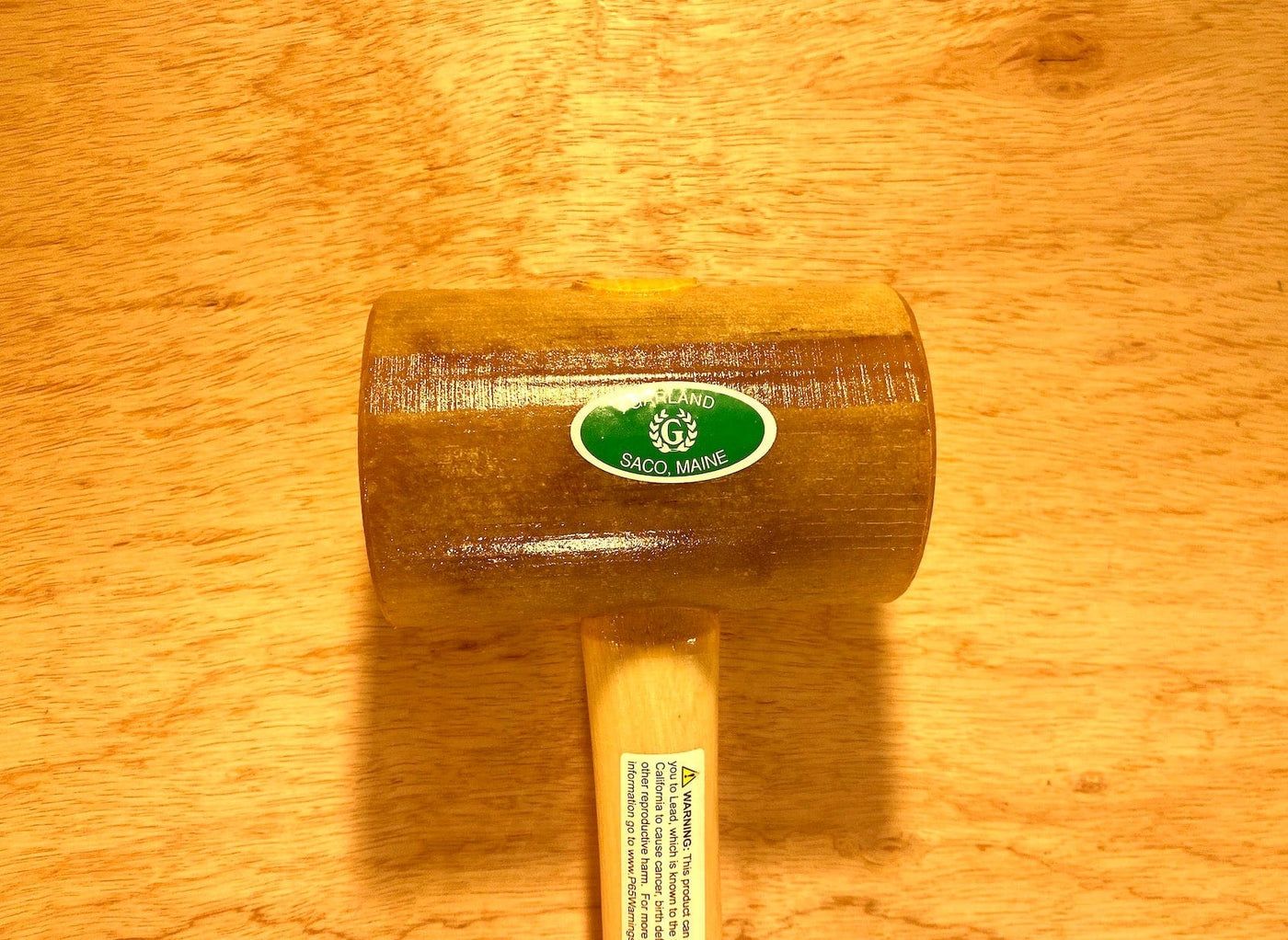 A Garland Weighted Rawhide Mallet from GAM lies flat on a wooden surface. It features a sticker labeled "Saco, Maine" on the head and is marked as 40 oz., proudly made in the USA.