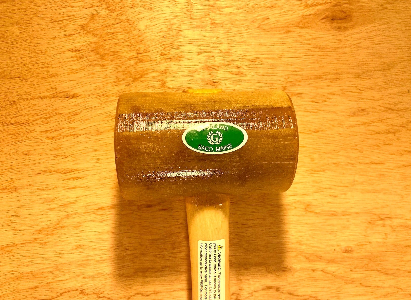 A Garland Weighted Rawhide Mallet from GAM lies flat on a wooden surface. It features a sticker labeled "Saco, Maine" on the head and is marked as 40 oz., proudly made in the USA.
