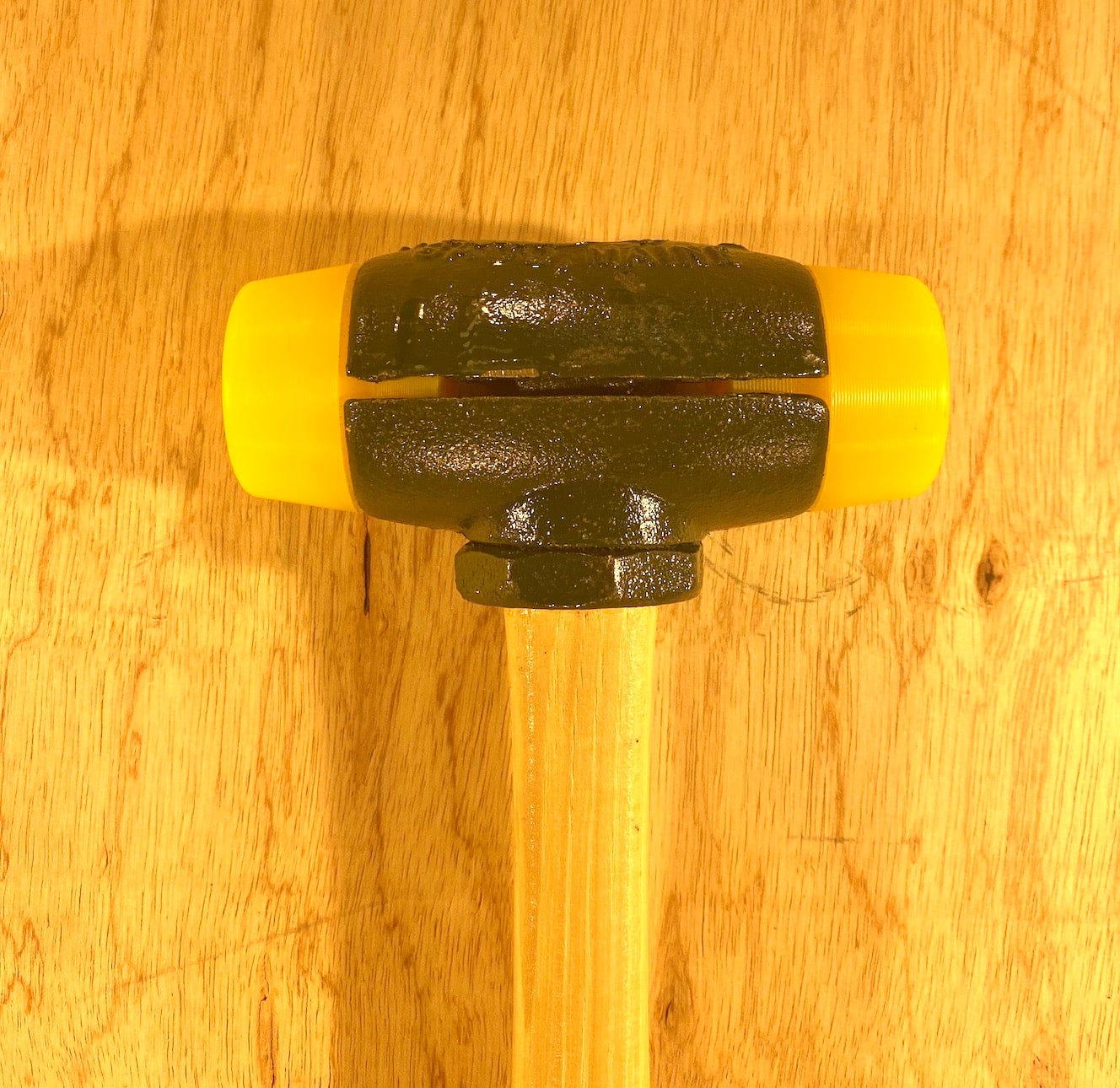 Close-up of a GAM Split Head Hammer Gar-Dur Face with a wooden handle and a yellow plastic-coated head, placed on a wooden surface.