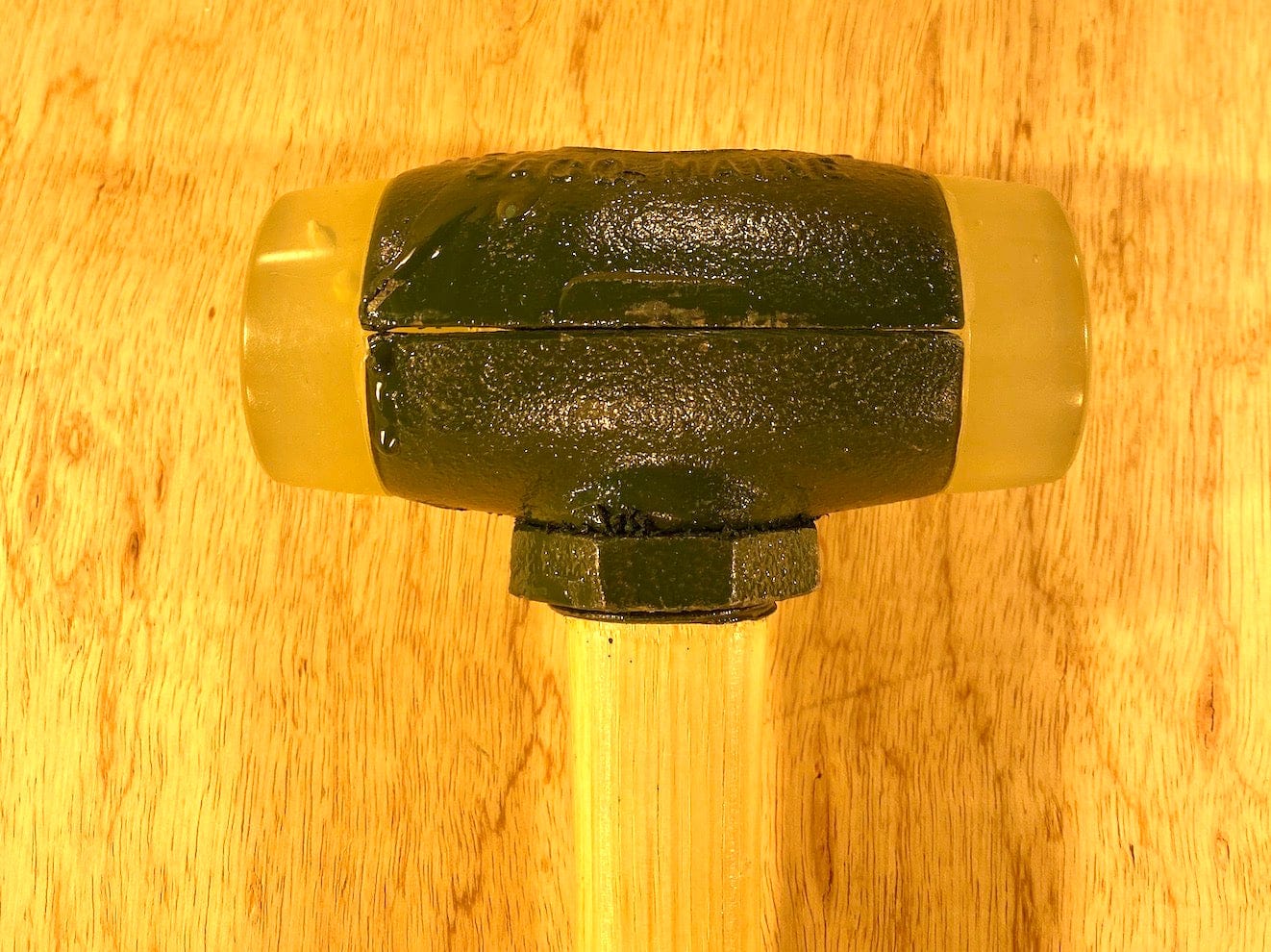 The Split Head Hammer Urethane Face by GAM, featuring interchangeable faces for versatile use, has a large metal head and a wooden handle, resting on a wooden surface.