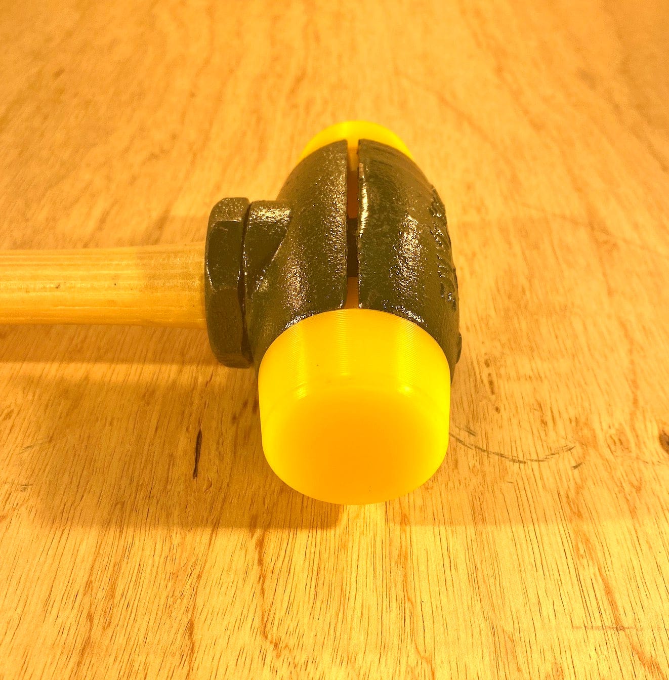 A close-up image of a GAM Split Head Hammer Gar-Dur Face, featuring a yellow and black rubber mallet head with interchangeable ultra-high-molecular-weight Gar-Dur plastic faces and a wooden handle, placed on a wooden surface.