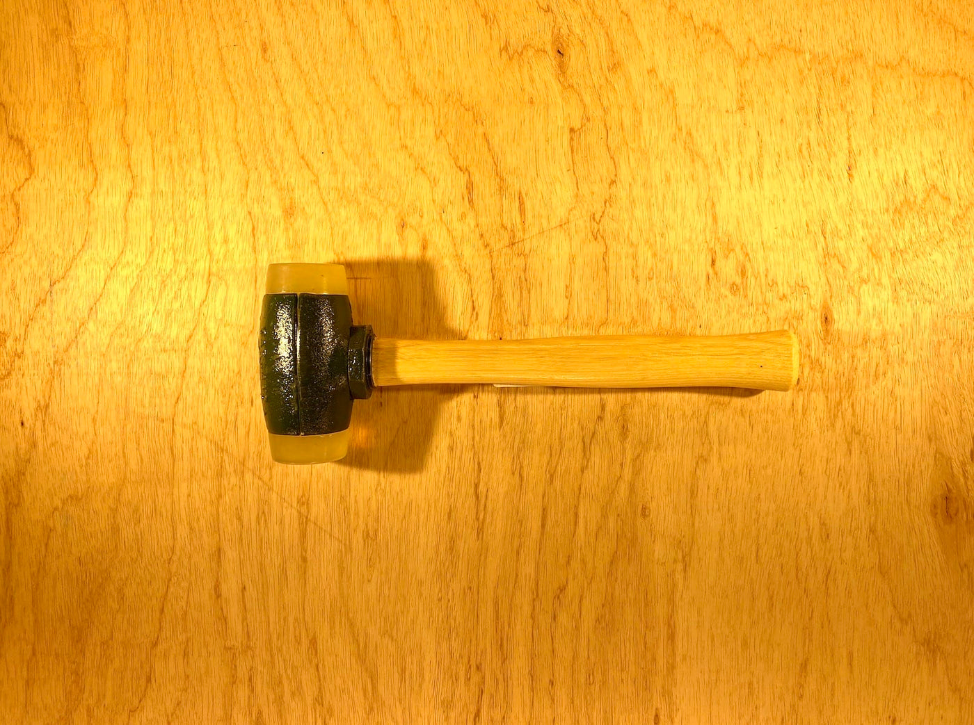 A Split Head Hammer Urethane Face with a wooden handle and dark metal head from GAM is on a wooden surface.