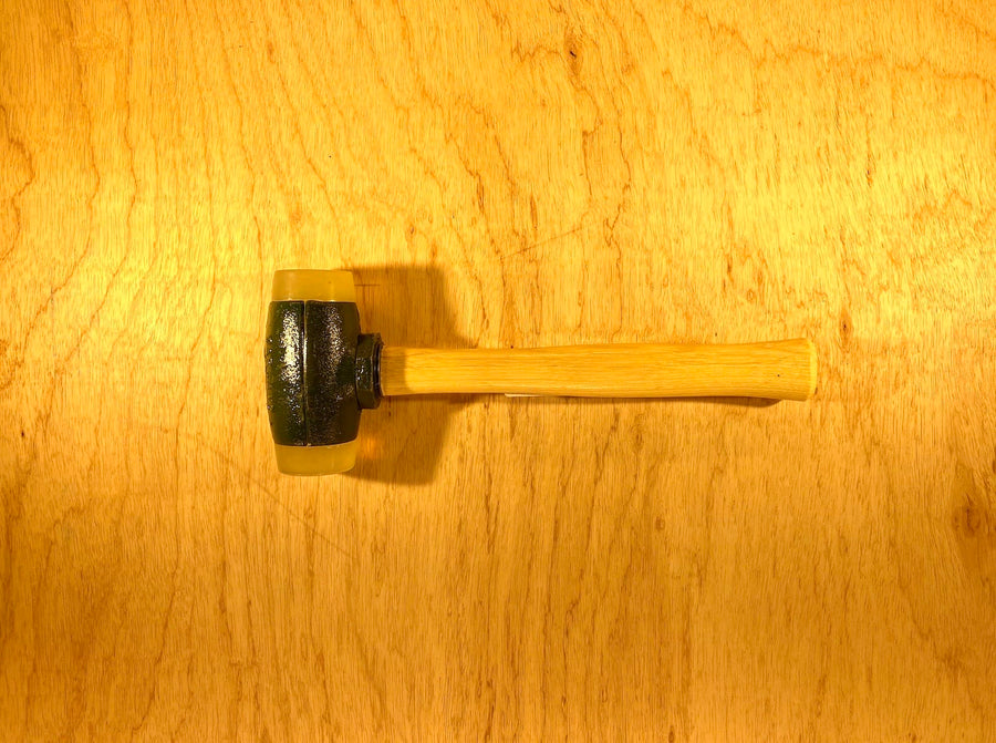 A Split Head Hammer Urethane Face with a wooden handle and dark metal head from GAM is on a wooden surface.