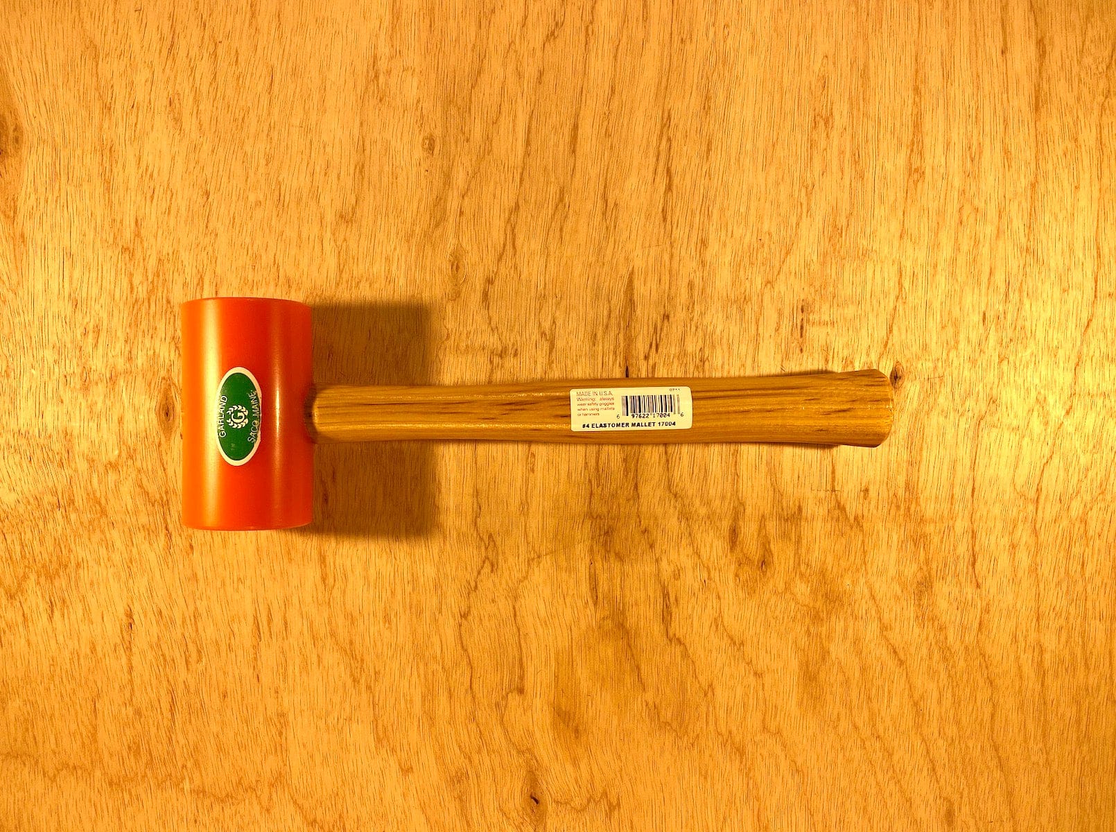 A Garland Elastomer Mallet with an orange head and wooden handle by GAM rests on a wooden surface, ideal for die-making applications.