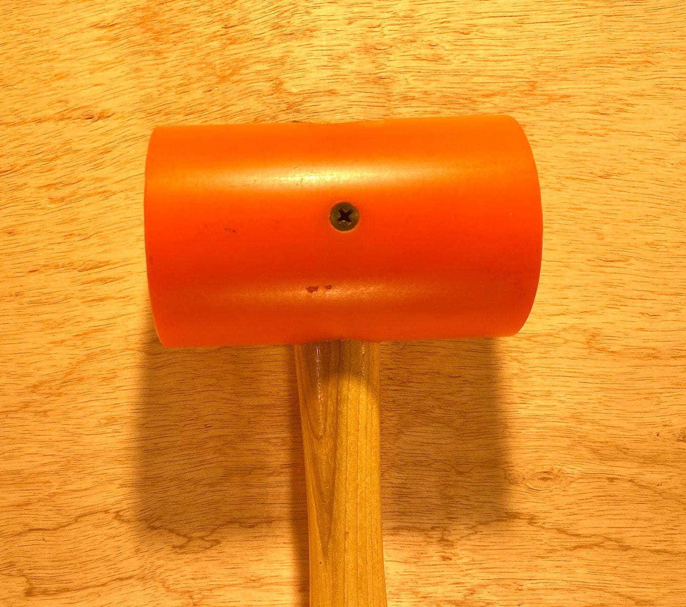 The GAM Garland Elastomer Mallet features a sturdy wooden handle and orange elastomer head, perfect for precision tasks and die-making applications, shown resting on a wooden surface.