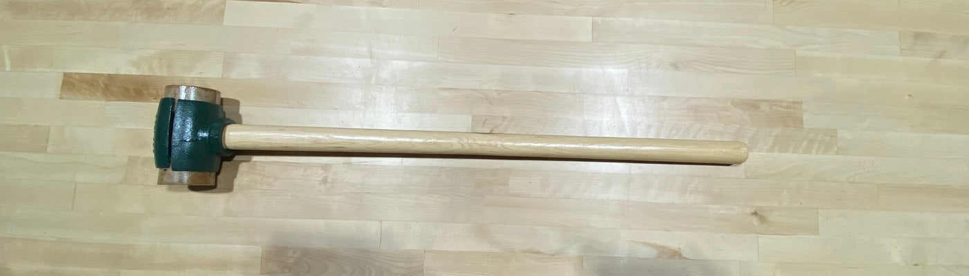 The Split Head Hammer Rawhide Face, featuring a green metal head and a light wooden handle, designed by GAM, rests on a light wood floor.