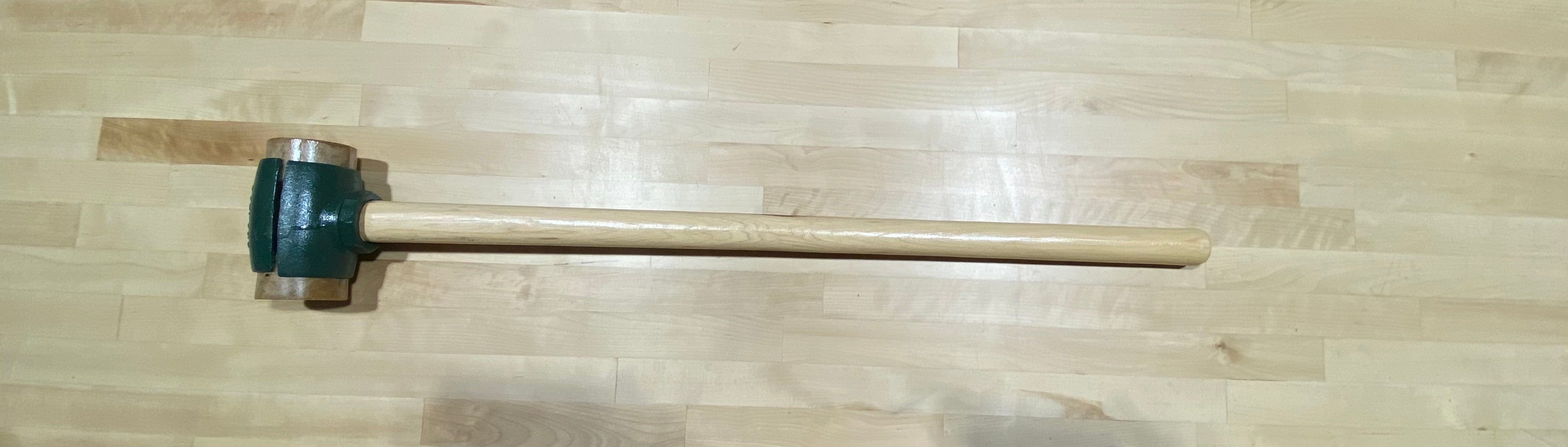 The Split Head Hammer Rawhide Face, featuring a green metal head and a light wooden handle, designed by GAM, rests on a light wood floor.