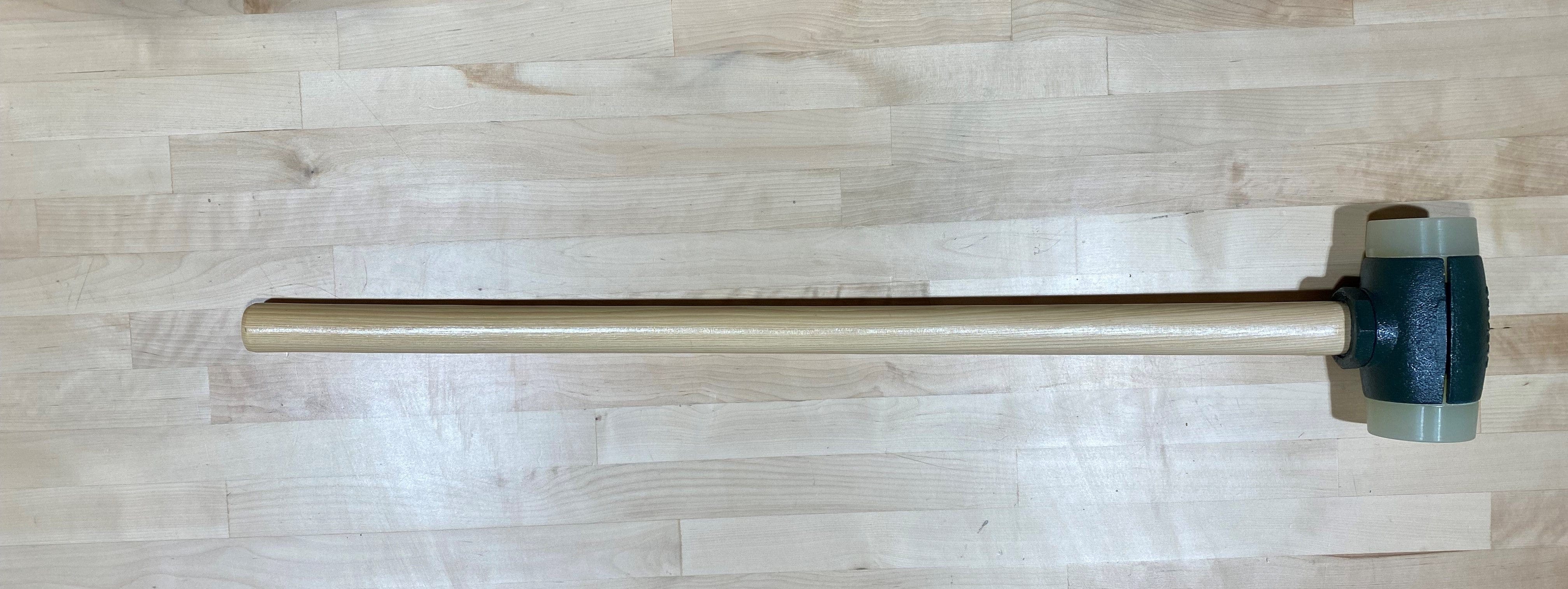 The Split Head Hammer Urethane Face by GAM, featuring a light wooden handle and dark rubber head, rests on a wooden surface.