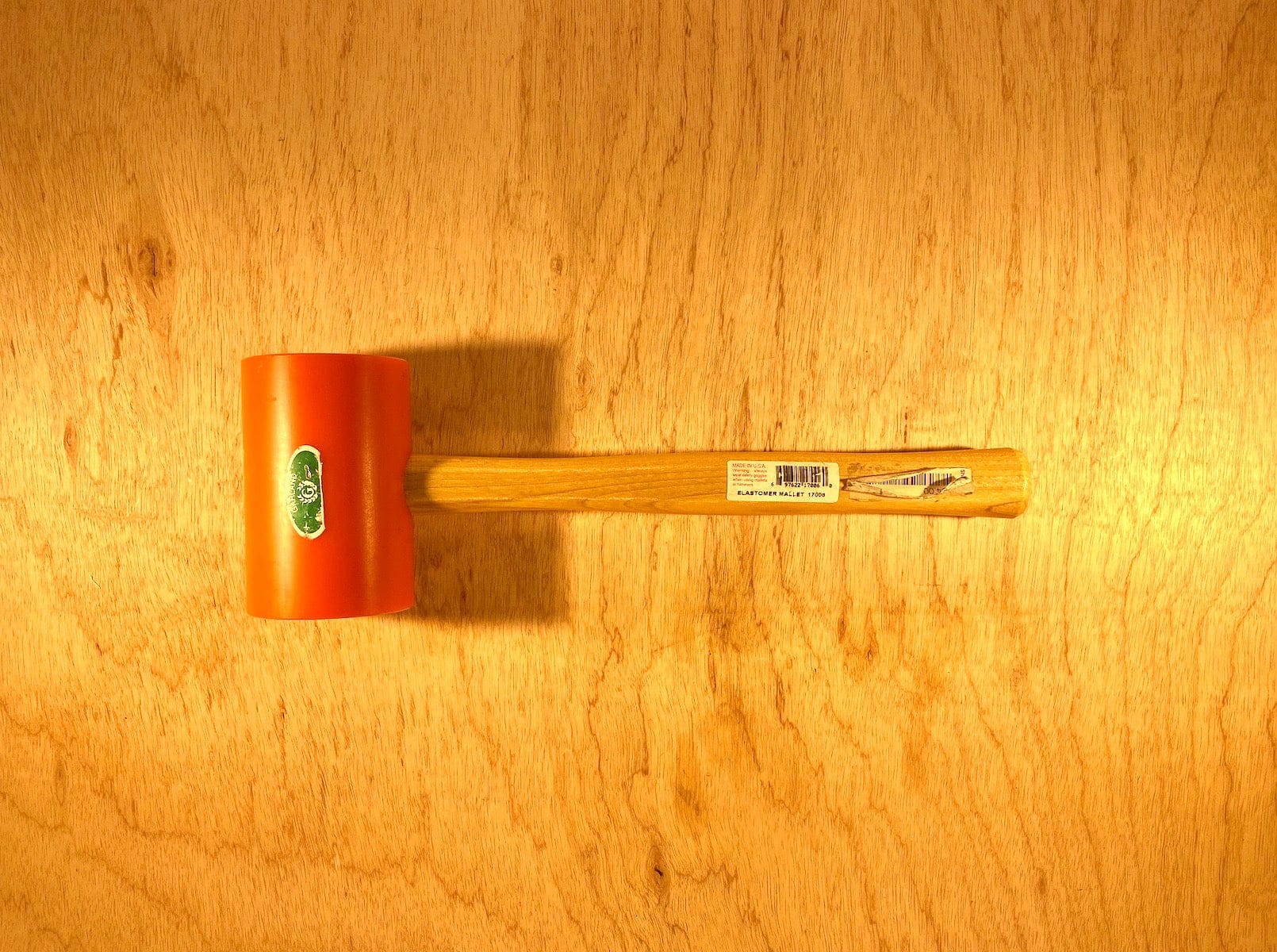 A GAM Garland Elastomer Mallet with an orange head and wooden handle is placed on a wooden surface, ideal for precise die-making applications.