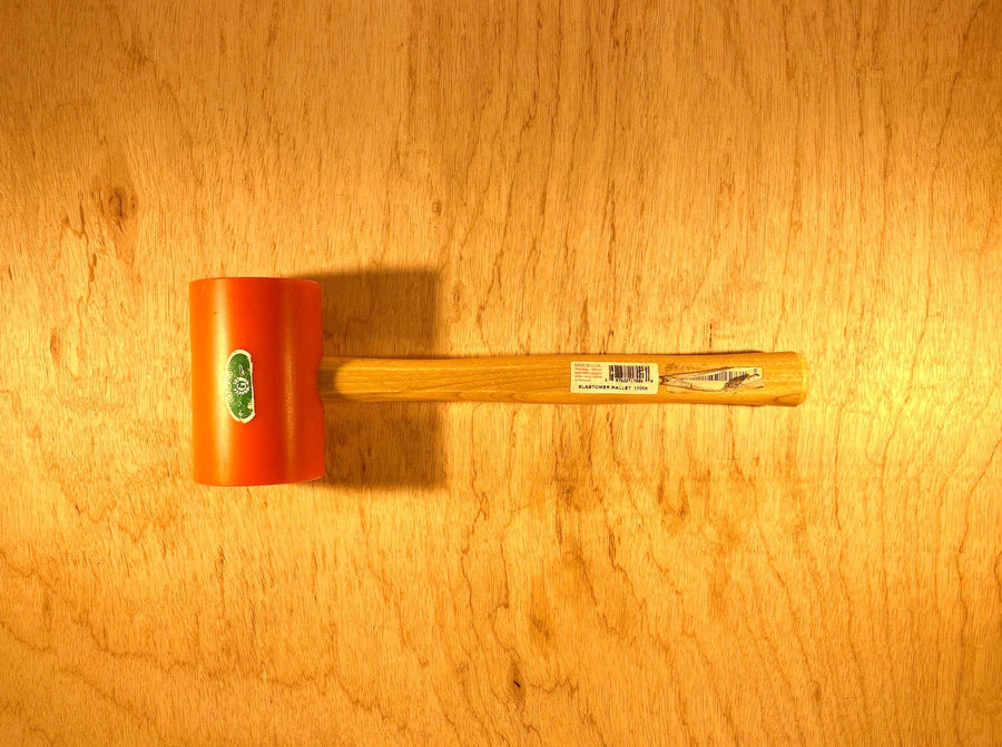 A GAM Garland Elastomer Mallet with an orange head and wooden handle is placed on a wooden surface, ideal for precise die-making applications.