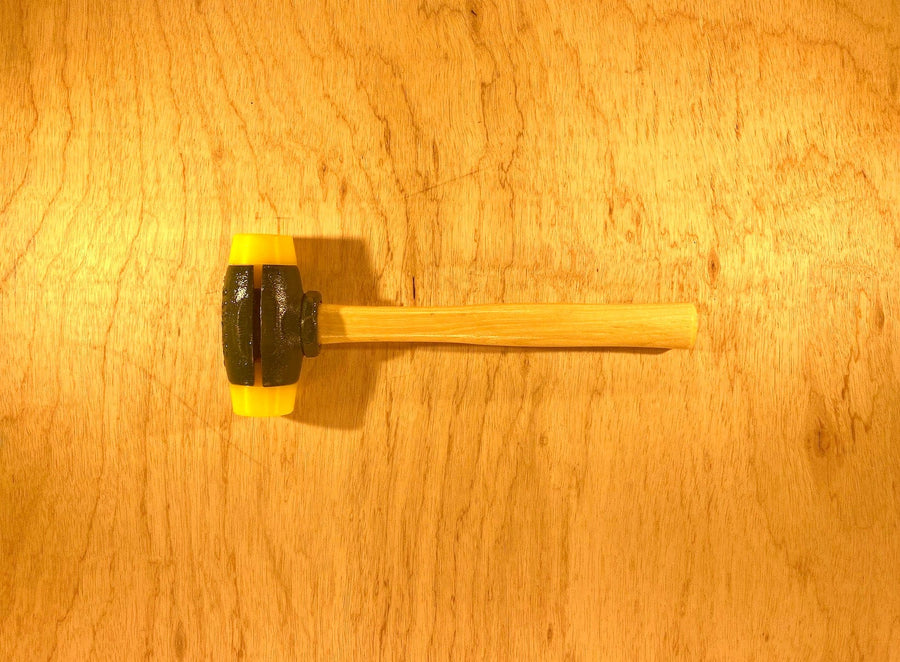 A Split Head Hammer Gar-Dur Face by GAM, featuring a wooden handle and a black and yellow rubber head made from ultra-high-molecular-weight Gar-Dur plastic, is placed on a wooden surface.