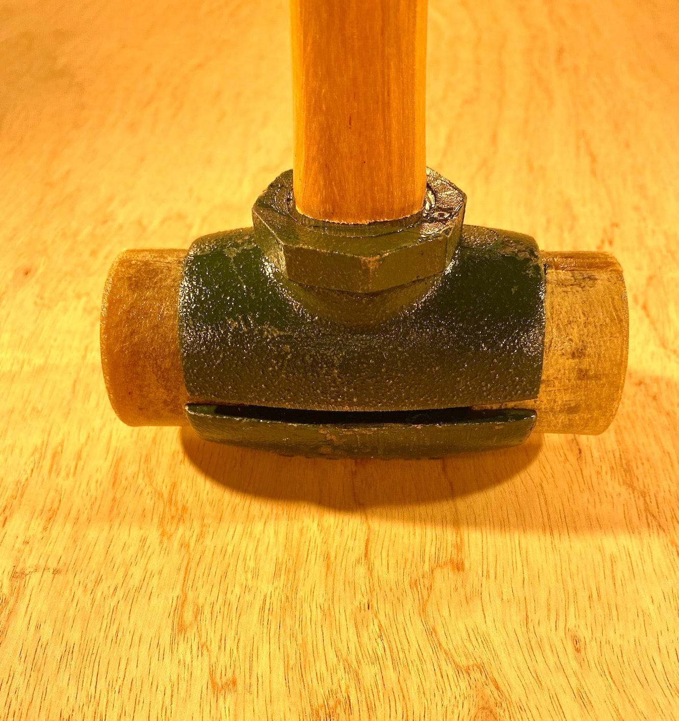 A close-up of a Split Head Hammer Rawhide Face with a wooden handle on a wooden surface, showcasing the metal details and wear marks. Crafted by GAM, this tool features robust construction and embodies the reliability synonymous with their name.