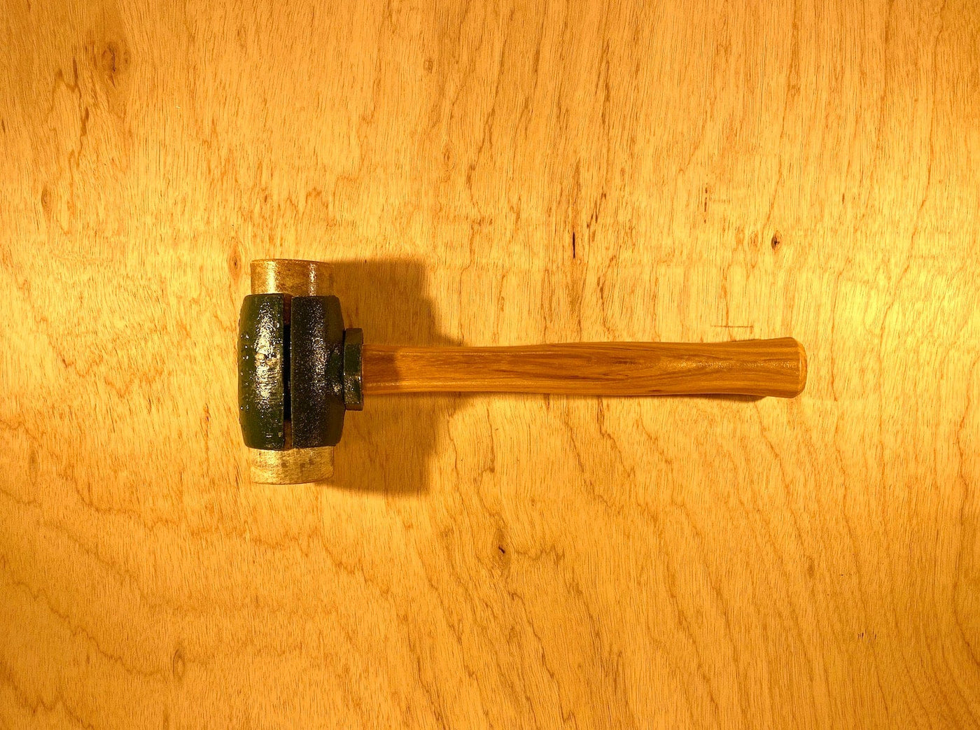 A finely crafted Split Head Hammer Rawhide Face with a wooden handle and a metal head from GAM rests on a light wood surface.