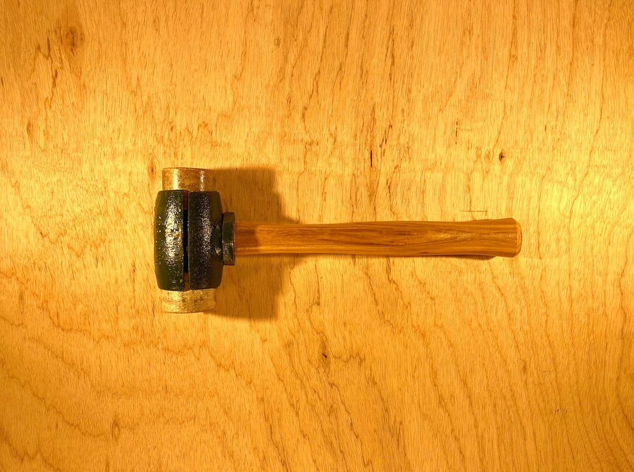 A finely crafted Split Head Hammer Rawhide Face with a wooden handle and a metal head from GAM rests on a light wood surface.
