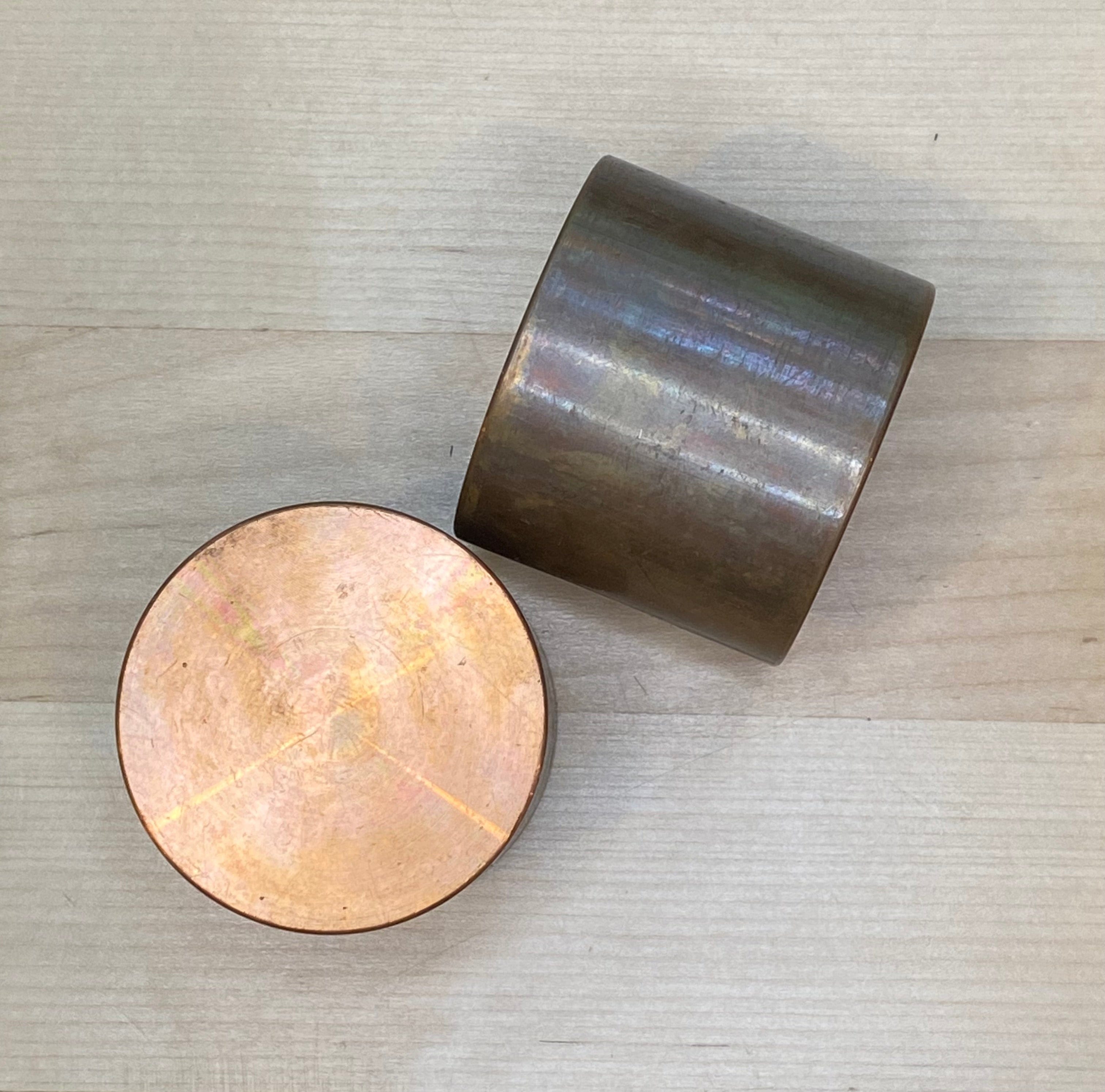 Two GAM Replacement Faces for Garland Mallets are displayed on a light wood surface. One stands upright, while the other lies on its side, showing its shiny copper-colored circular end.