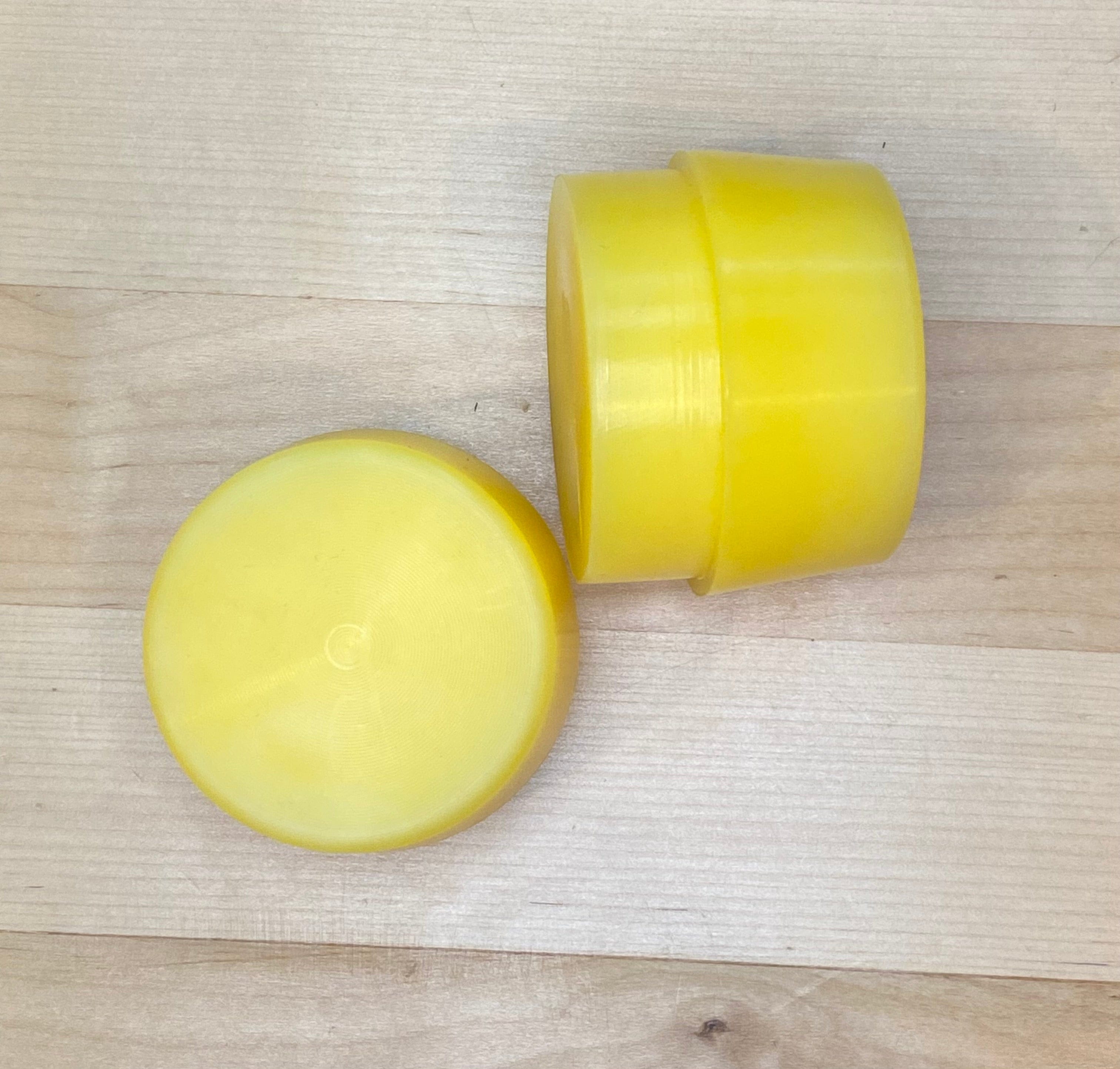 Two round yellow solid bars from GAM, designed as Replacement Faces for Garland Mallets, rest on a light wooden surface—one upright, one lying down—both featuring smooth, shiny finishes.