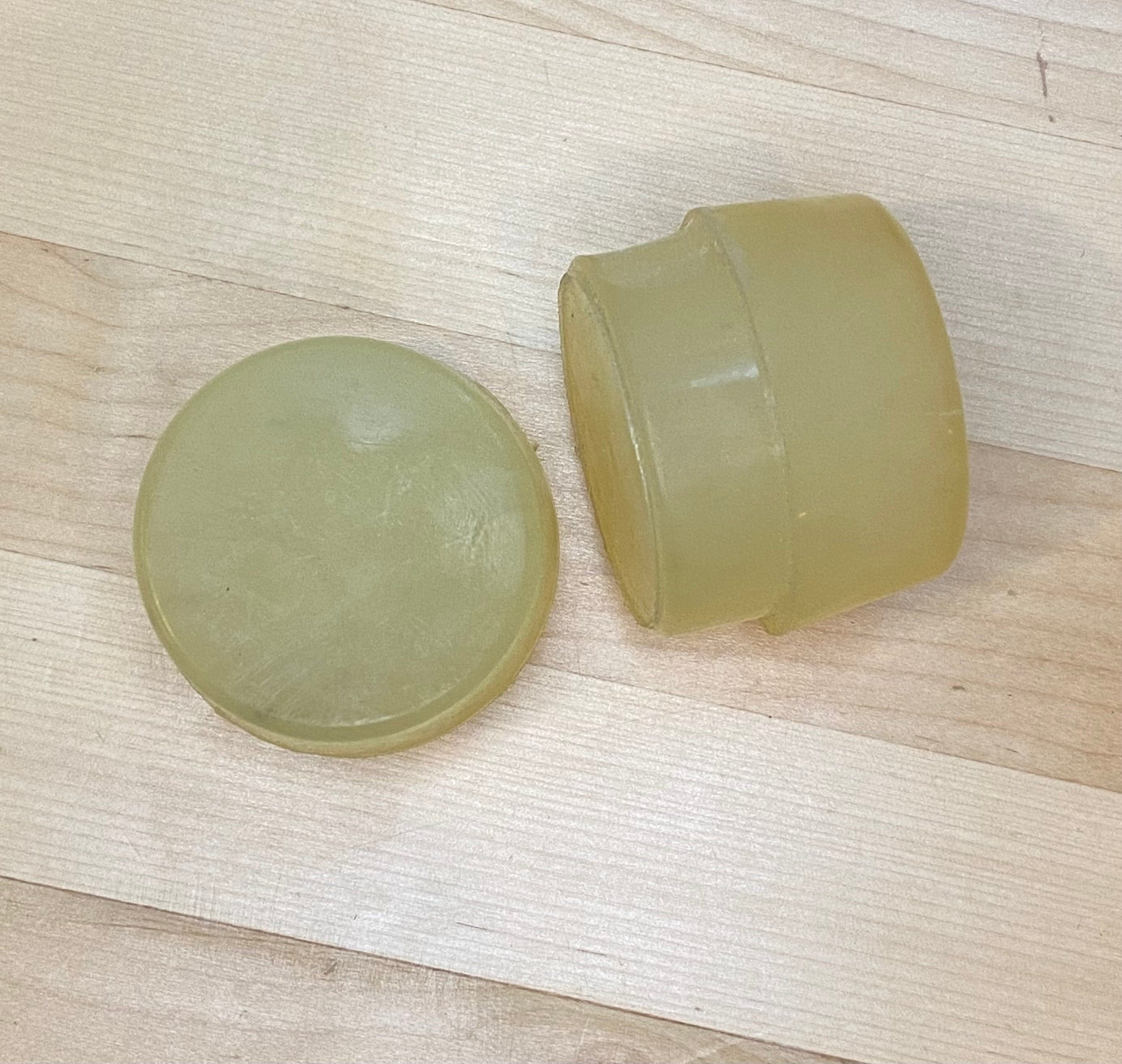 Two round, yellowish Replacement Faces for Garland Mallets by GAM are displayed on a light wooden surface—one upright and one flat—showcasing both the side and top views.