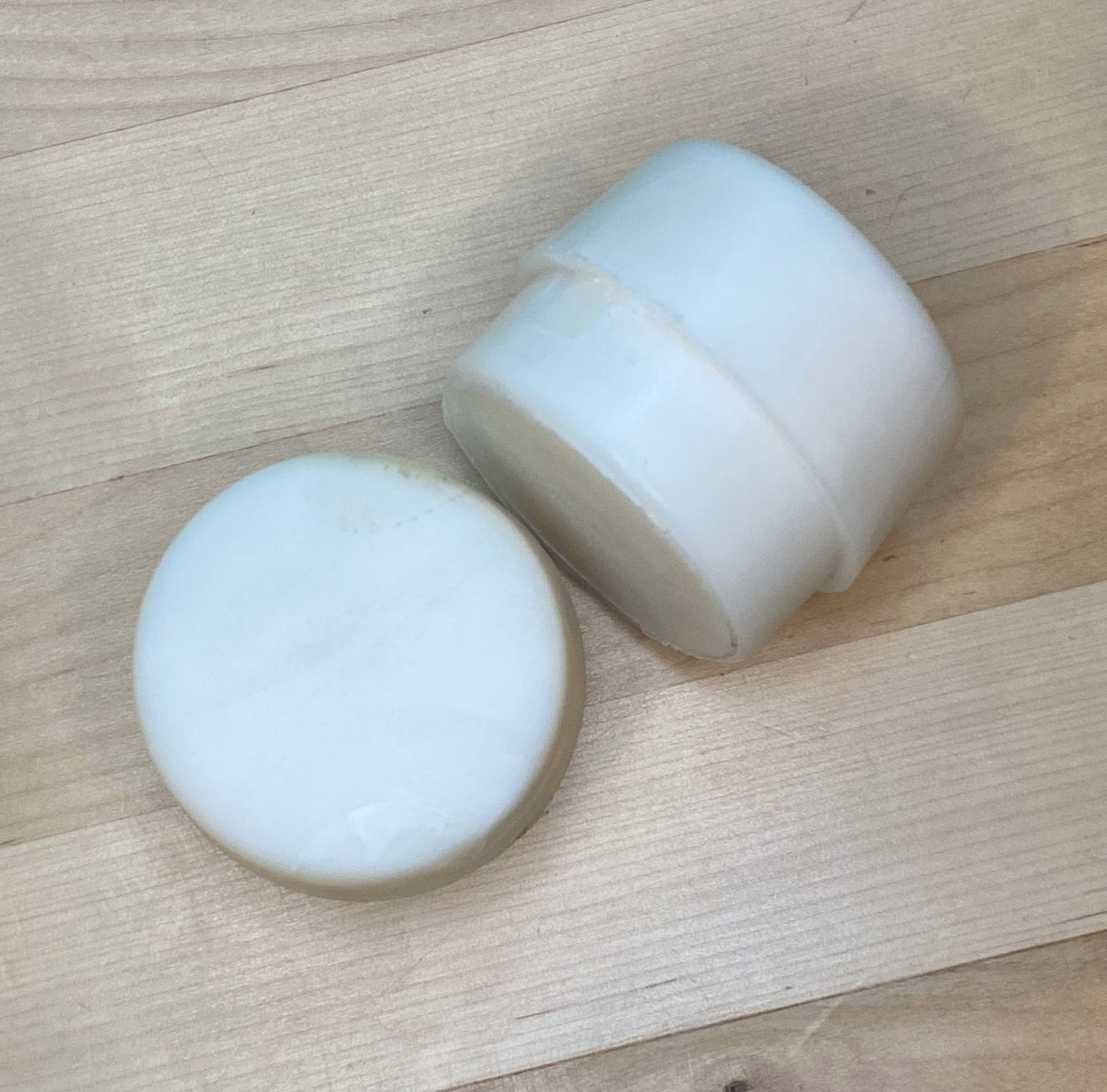Two white, cylindrical GAM Replacement Faces for Garland Mallets rest on a light wooden surface—one upright, the other lying flat to show its smooth, round top.