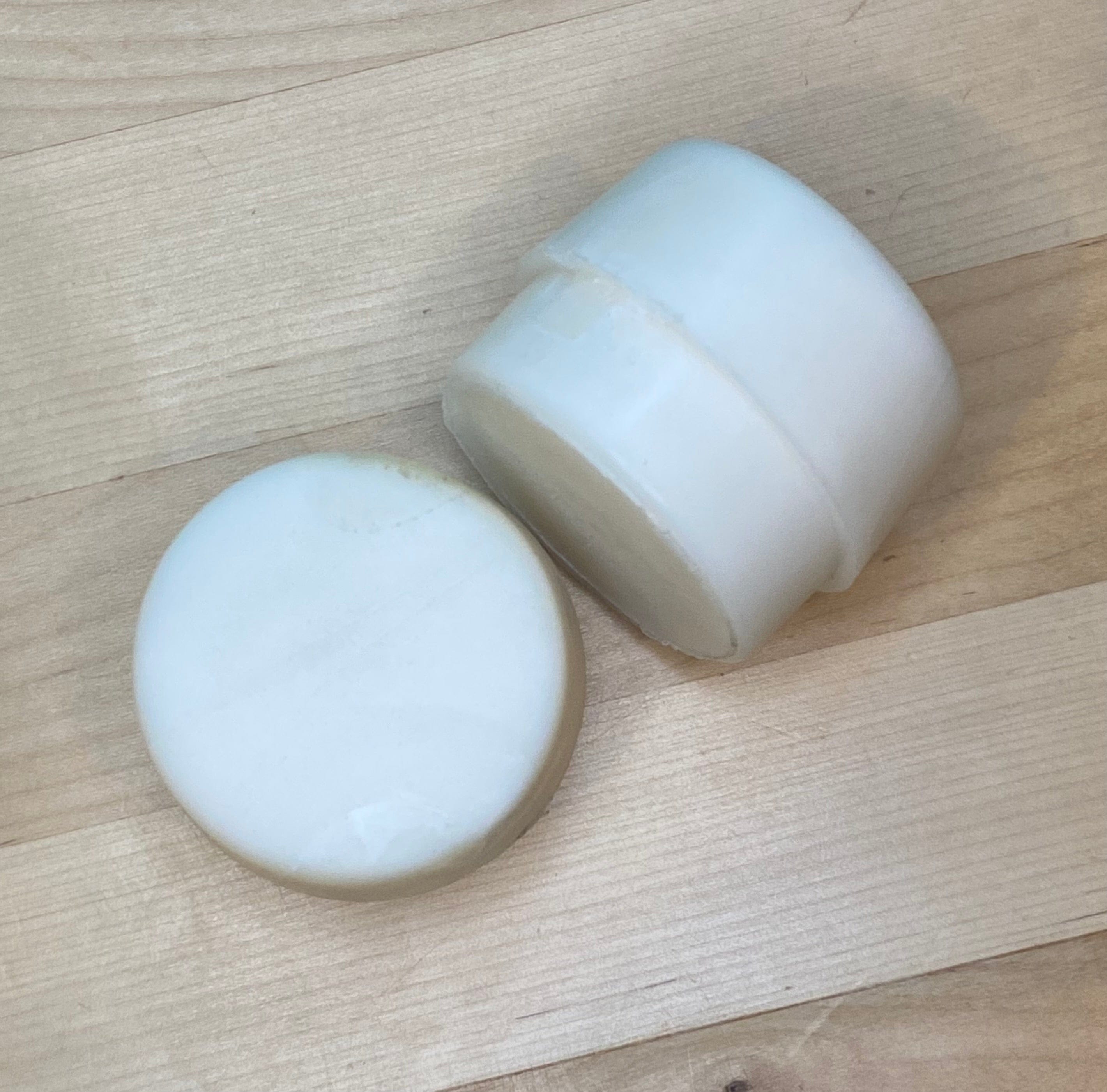 Two white, cylindrical GAM Replacement Faces for Garland Mallets rest on a light wooden surface—one upright, the other lying flat to show its smooth, round top.