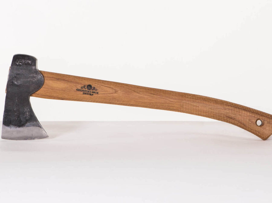 The GRF Gransfors Bruk Hunters Axe 418 features a smooth, curved wooden handle with a storage hole and a worn metal head, lying flat on a white surface—ideal for chopping wood.