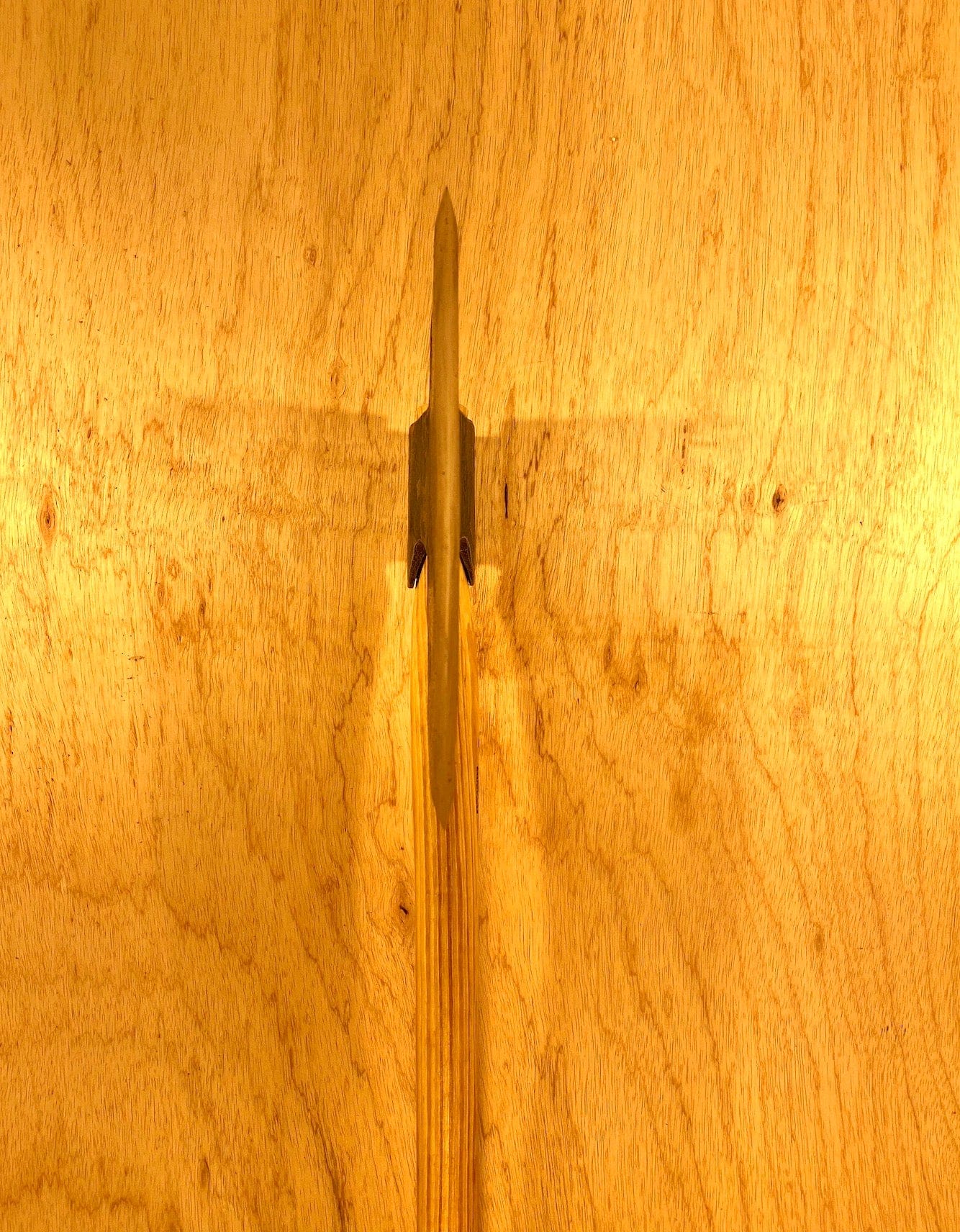 A Gransfors Bruk Broad Axe by GRF with a metal blade embedded in a wooden surface, casting a shadow reminiscent of the tools used in timber hewing during log house building.