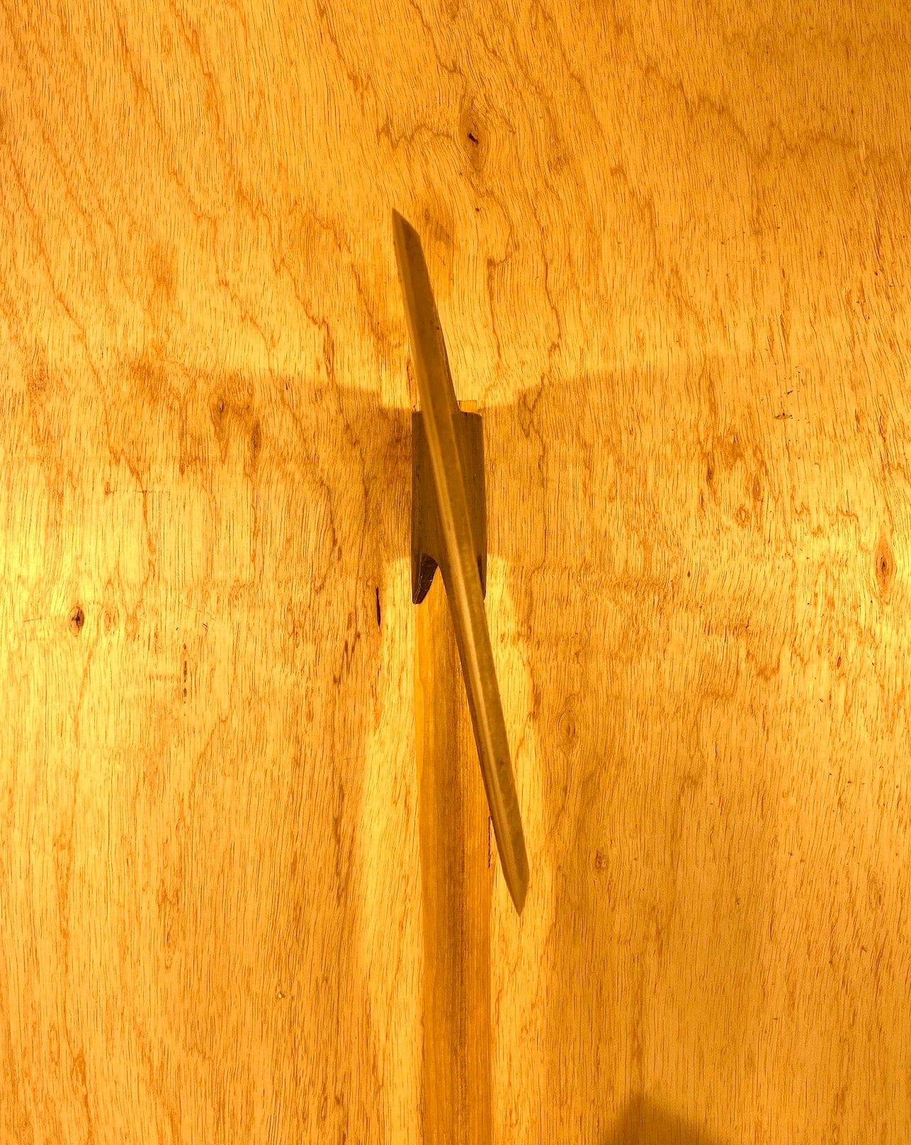 A Gransfors Bruk Broad Axe by GRF, reminiscent of fine timber craftsmanship, is mounted on a wooden wall with a warm yellow lighting effect, evoking the coziness of a log house.