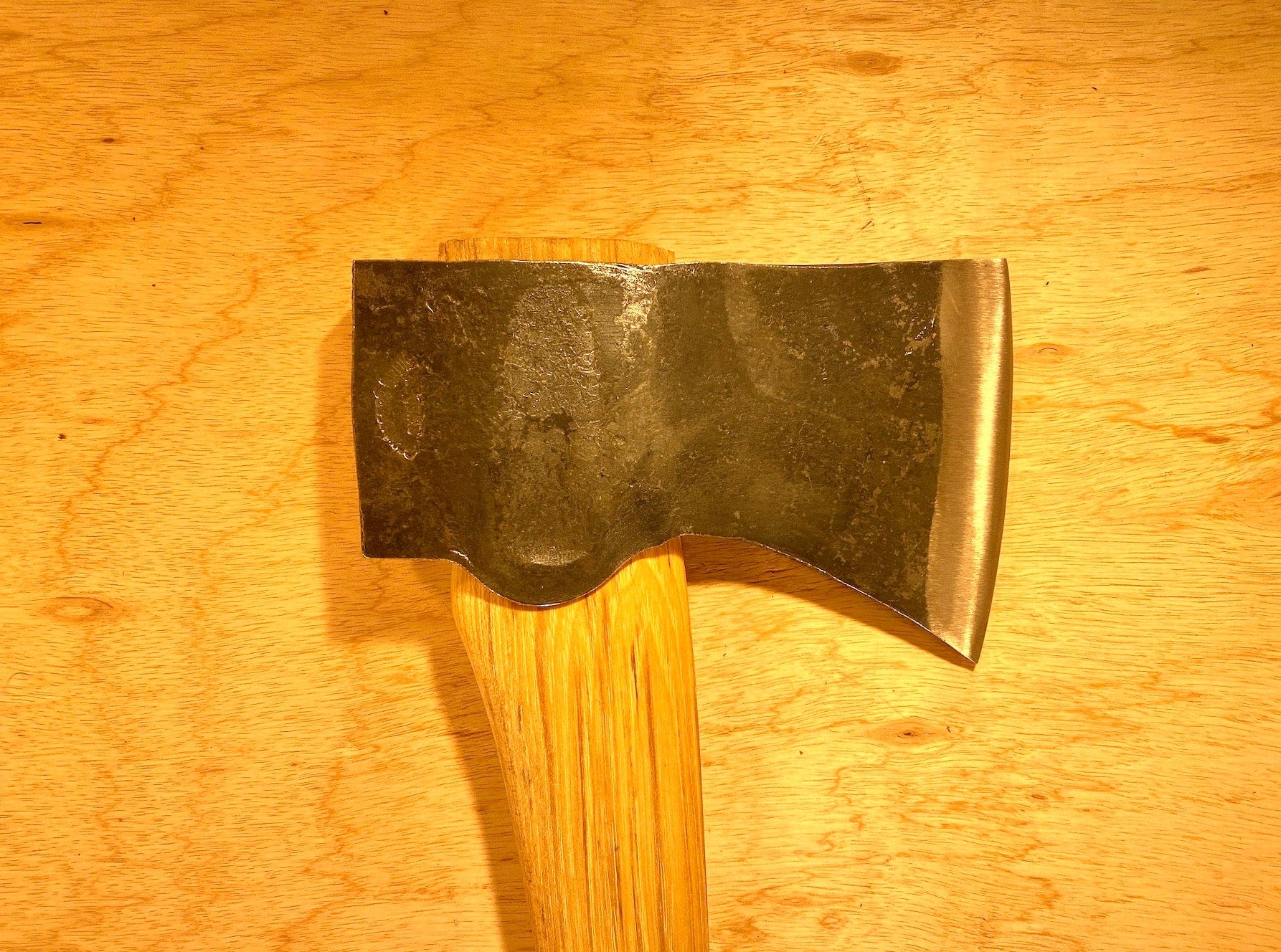 The Gransfors Bruk American Felling Axe by GRF, featuring a Swedish-crafted metal axe head and a 35-inch wooden handle, rests on a wooden surface.