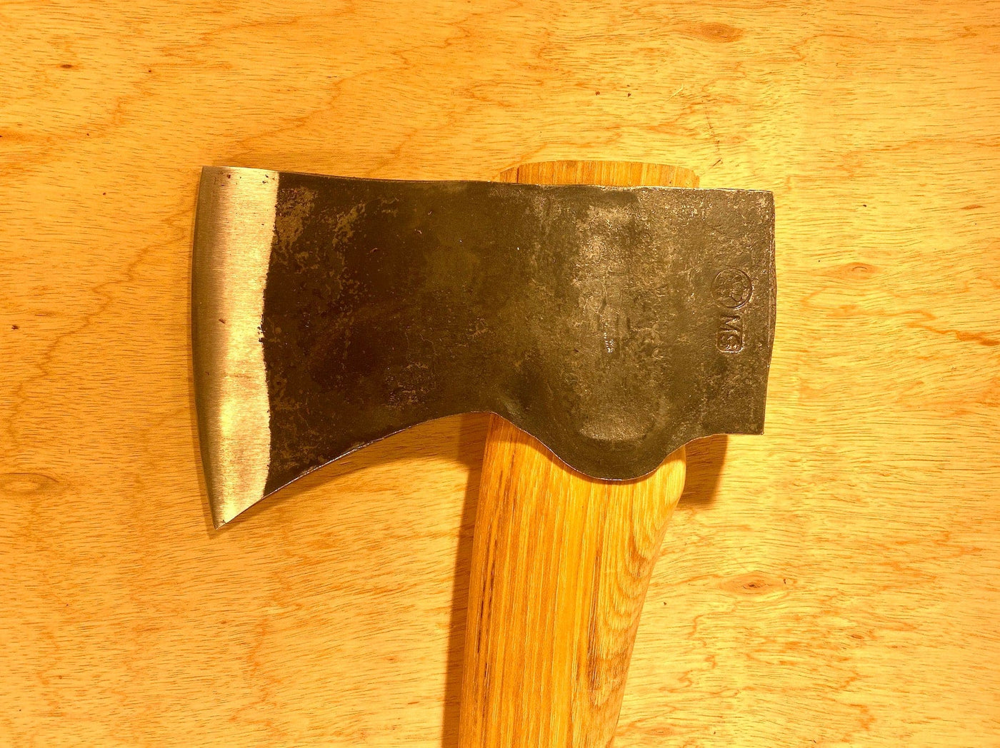 A close-up of a GRF Gransfors Bruk American Felling Axe with a 35-inch wooden handle on a wooden surface, highlighting traditional forestry techniques.
