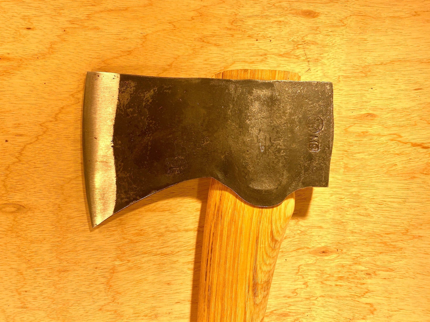 A close-up of a GRF Gransfors Bruk American Felling Axe with a 35-inch wooden handle on a wooden surface, highlighting traditional forestry techniques.