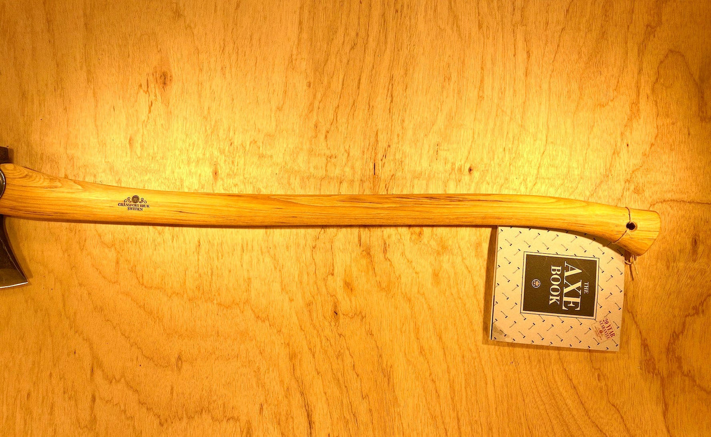 A Gransfors Bruk American Felling Axe with a 35-inch handle rests on wood, showcasing Swedish craftsmanship. A label reads "Axe Book.