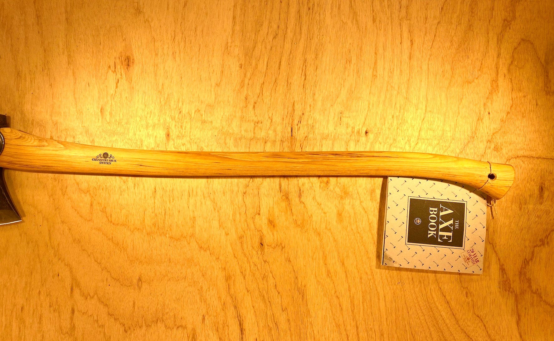 A Gransfors Bruk American Felling Axe with a 35-inch handle rests on wood, showcasing Swedish craftsmanship. A label reads "Axe Book.