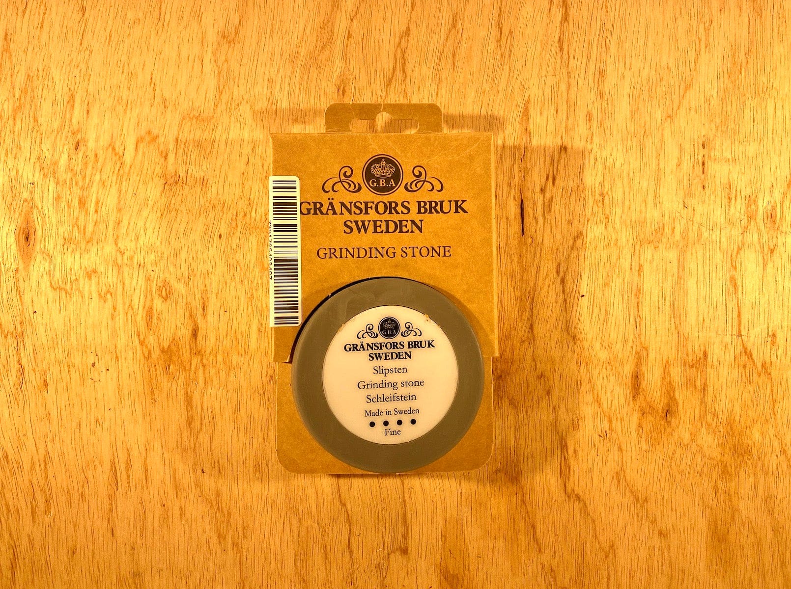 The Gransfors Bruk Ceramic Sharpening Stone by GRF is a precision tool packaged in a cardboard box labeled "Gränsfors Bruk Sweden Grinding Stone," resting on a wooden surface.