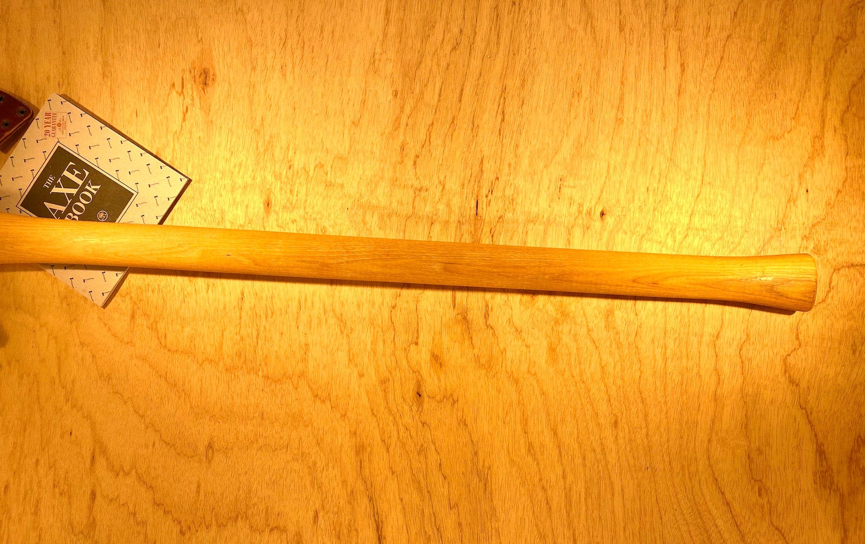 A GRF Gransfors Bruk Double Bit Axe 35in Handle rests elegantly on a light-colored wooden surface, with a small booklet partially visible underneath one end – ideal for those passionate about axe throwing.