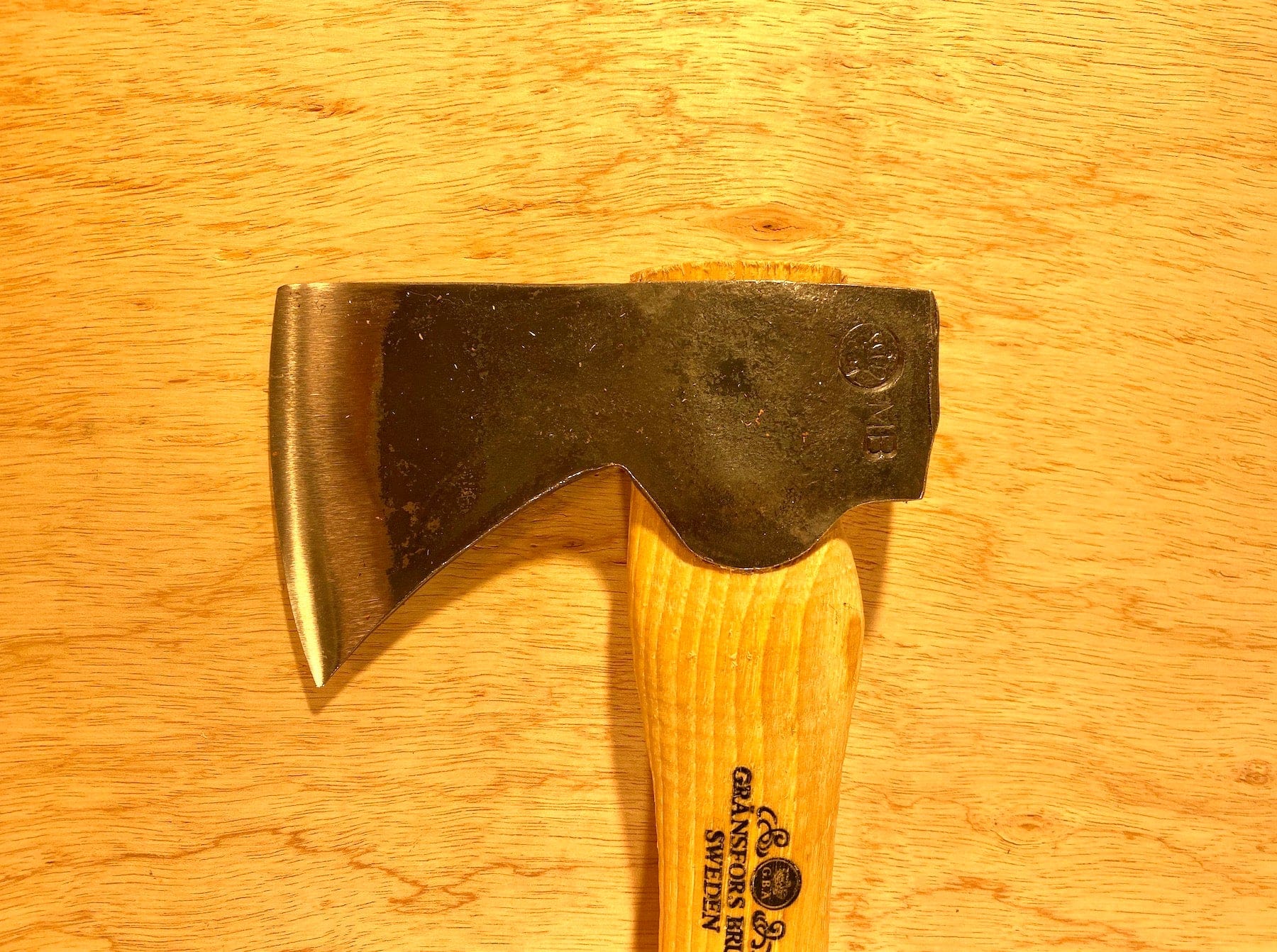 A Gransfors Bruk Hand Hatchet 413 from GRF, featuring a steel axe head with a wooden handle engraved "Gränsfors Bruk Sweden," ideal for scouting and camping trips, placed on a wooden surface.
