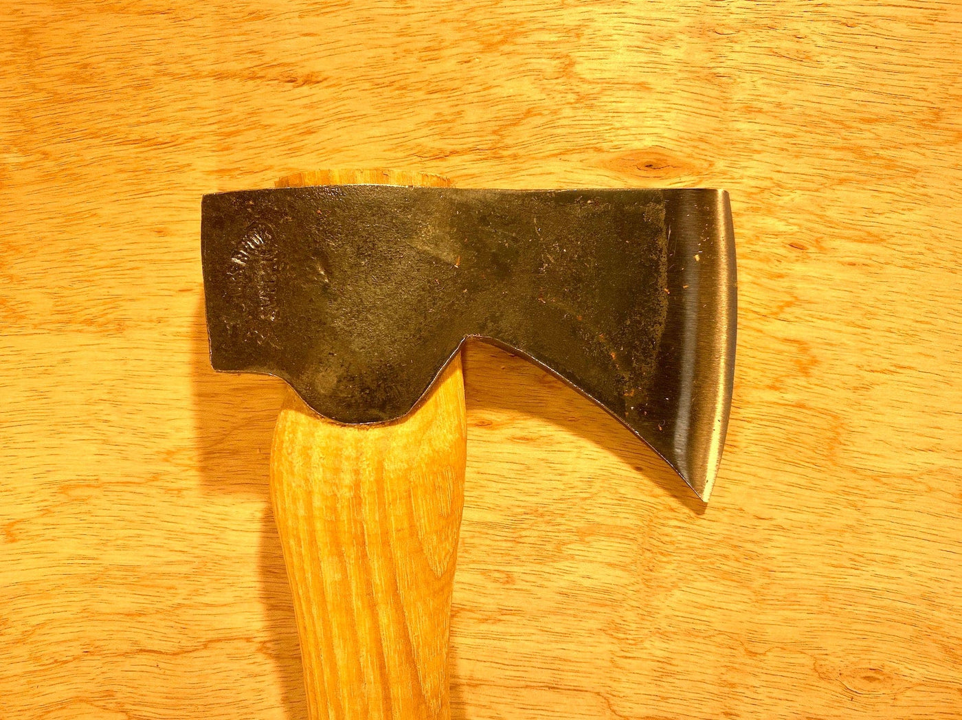 The Gransfors Bruk Hand Hatchet 413 by GRF, a quintessential scouting and camping axe, features a metal head with a smooth wooden handle, resting on an unvarnished wooden surface. Perfect for splitting firewood.