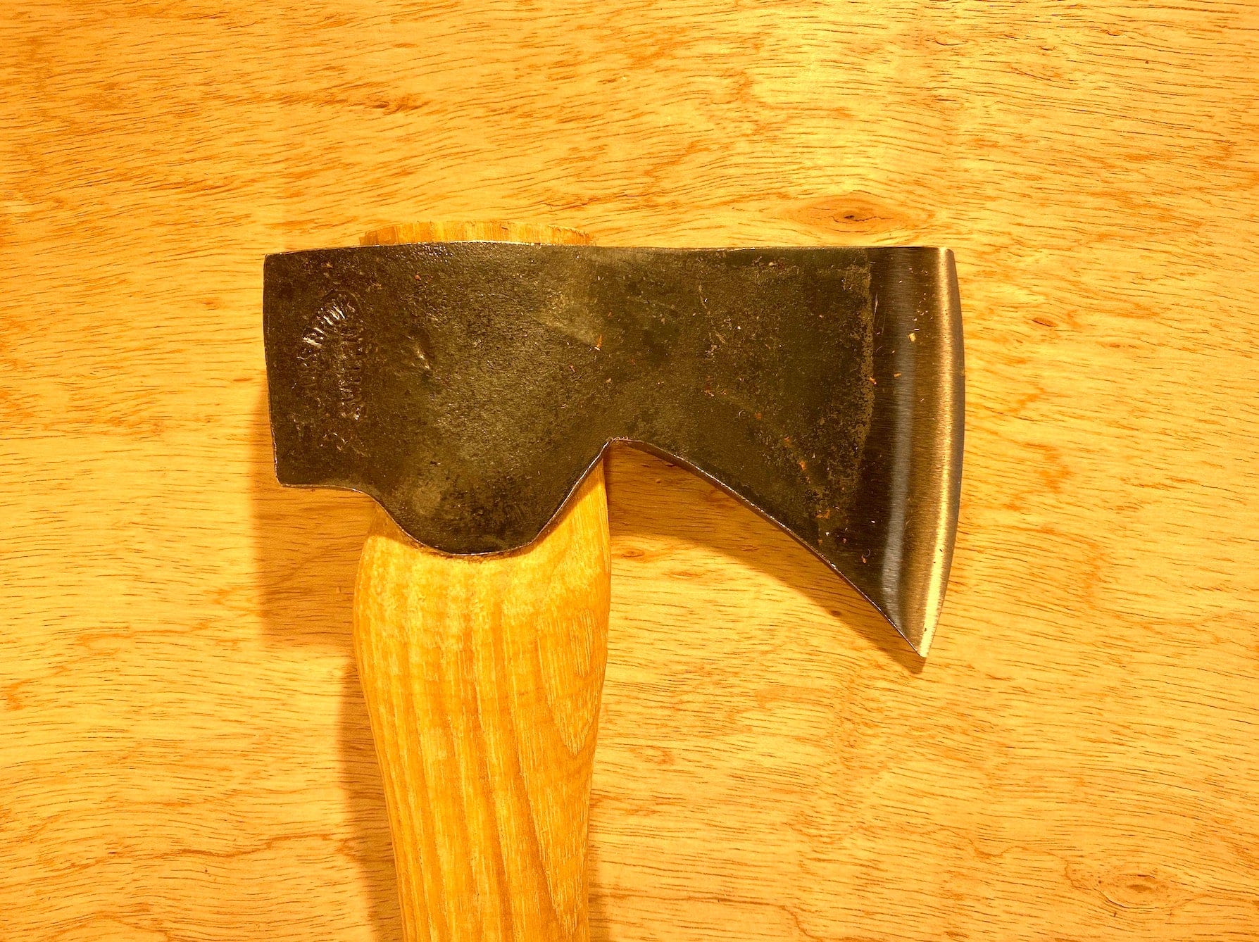 The Gransfors Bruk Hand Hatchet 413 by GRF, a quintessential scouting and camping axe, features a metal head with a smooth wooden handle, resting on an unvarnished wooden surface. Perfect for splitting firewood.