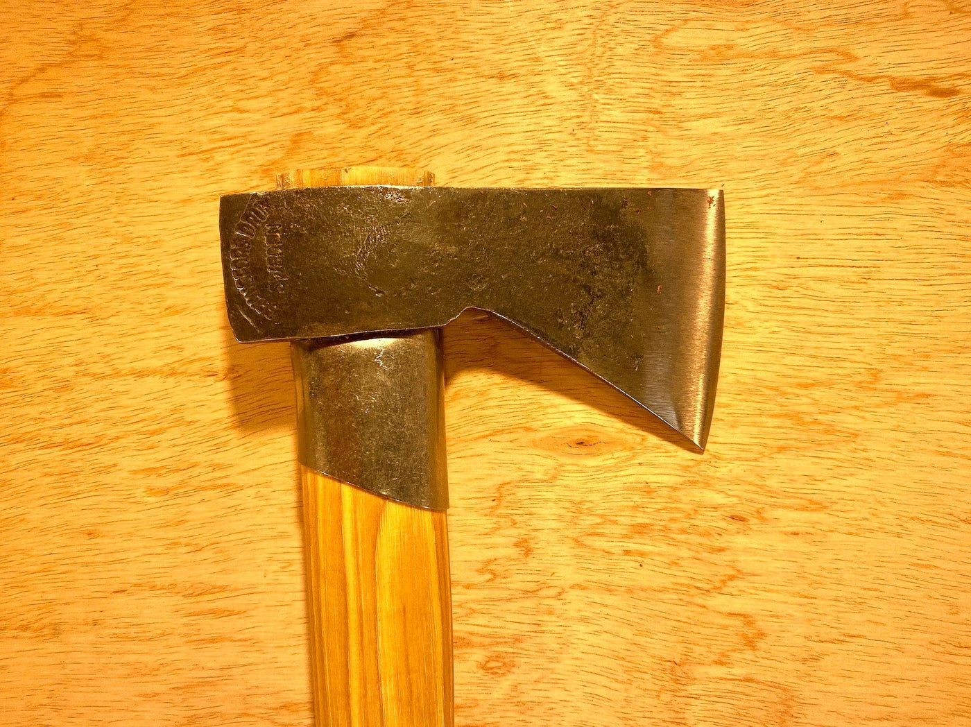 The Gransfors Bruk Outdoor Axe by GRF, featuring a metallic head and wooden handle, rests on a wooden surface, showcasing the craftsmanship admired by survival experts.