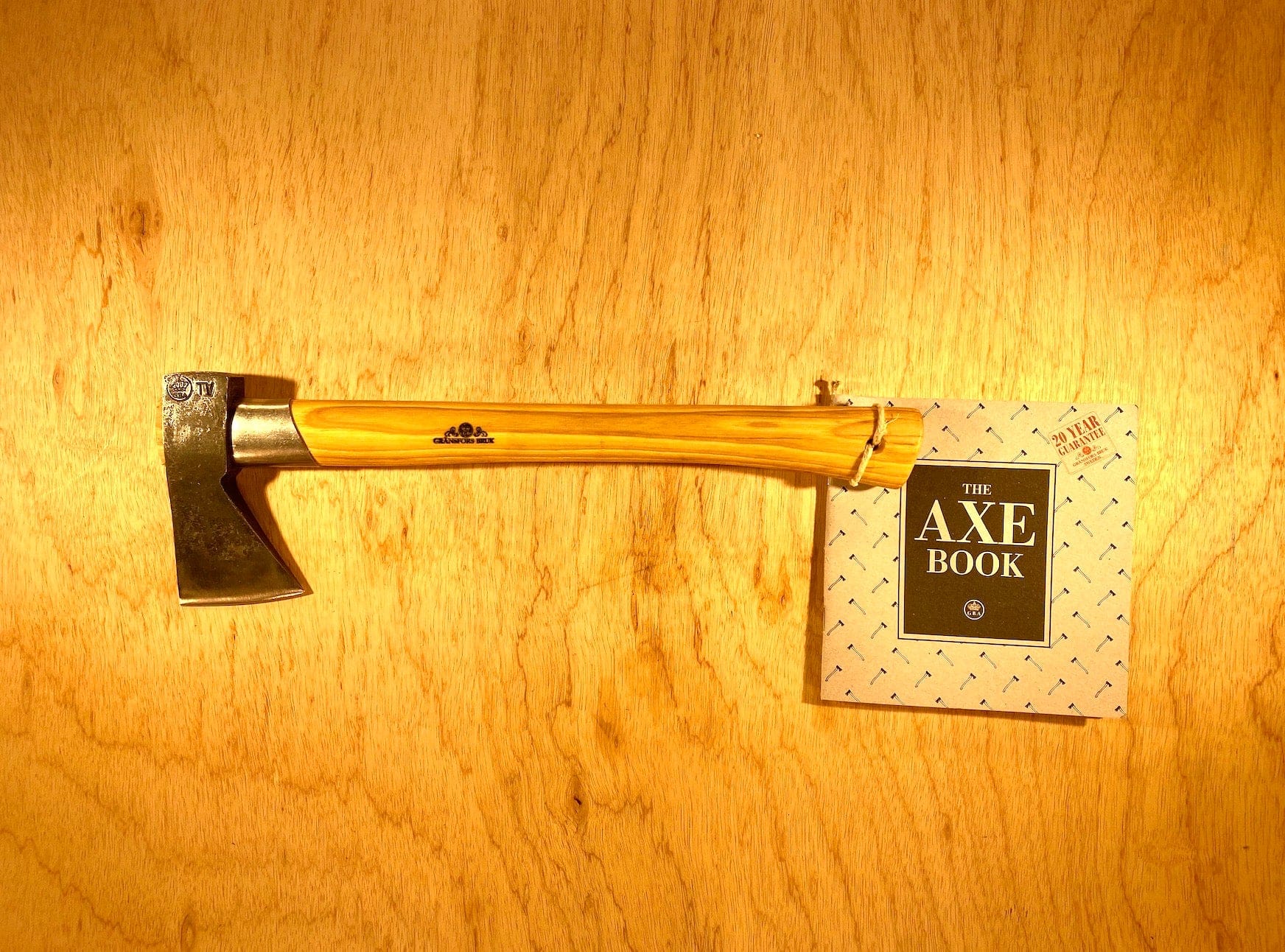 A GRF Gransfors Bruk Outdoor Axe with a wooden handle lies on a timber surface next to "The Axe Book." Renowned survival expert Lars Fält, known for his work at the Swedish Armed Forces Survival School, would definitely recommend this gear for wilderness adventures.