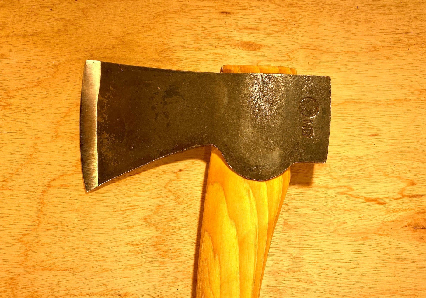 Close-up of a GRF Gransfors Bruk Scandinavian Forest Axe featuring a wooden handle and a black metal head resting on a wooden surface, highlighting its design as a professional forestry tool perfect for felling and limbing.