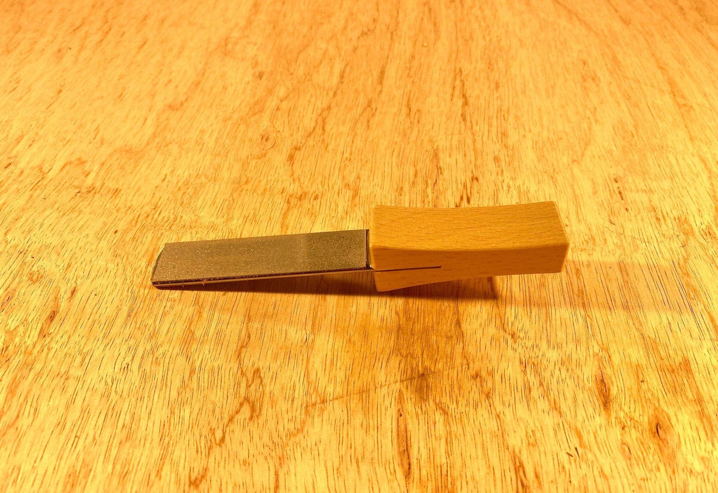 A Gransfors Bruk Sharpening Diamond File from GRF, featuring a sturdy wooden handle, lies flat on a wooden surface.